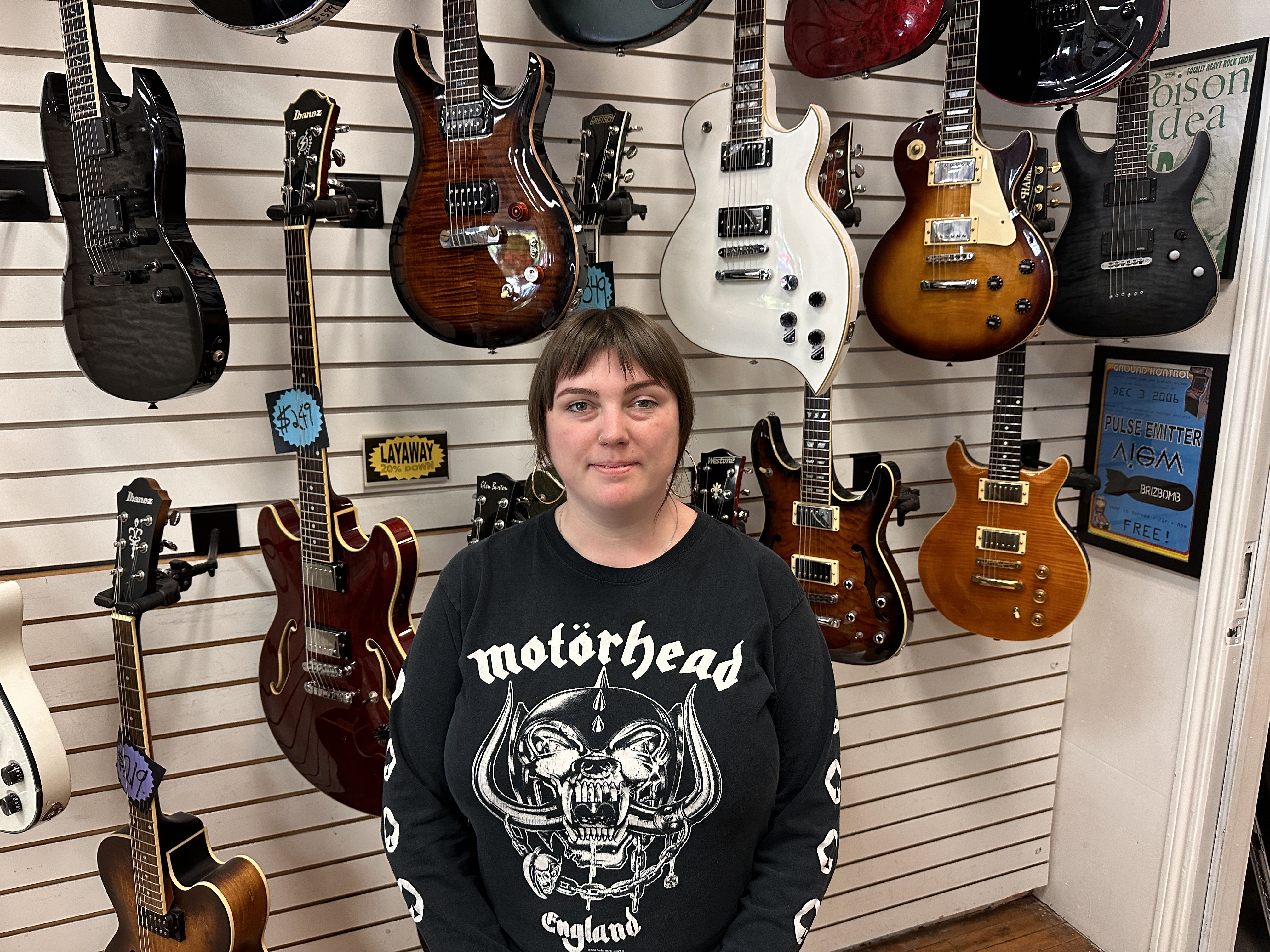 Woman in Motorhead t-shirt in front of hanging guitars for sale
