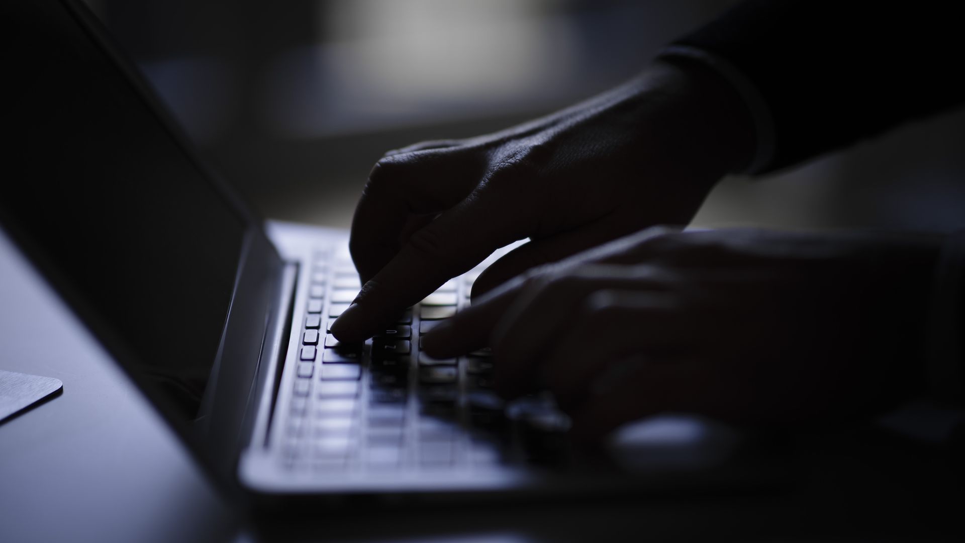 Hands tap on laptop keyboard in darkness