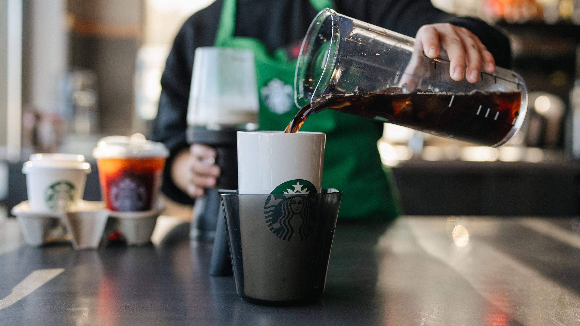 Starbucks barista pours coffee in a reusable cup for a take-out order.