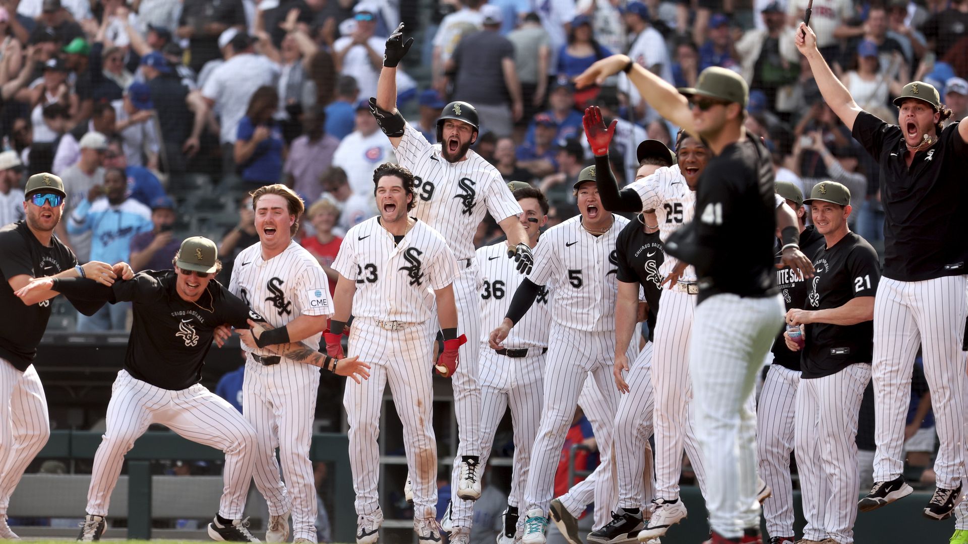 Baseball players in white pinstripe Chicago White Sox uniforms celebrate on the field, arms raised amid a cheering crowd in the stands.