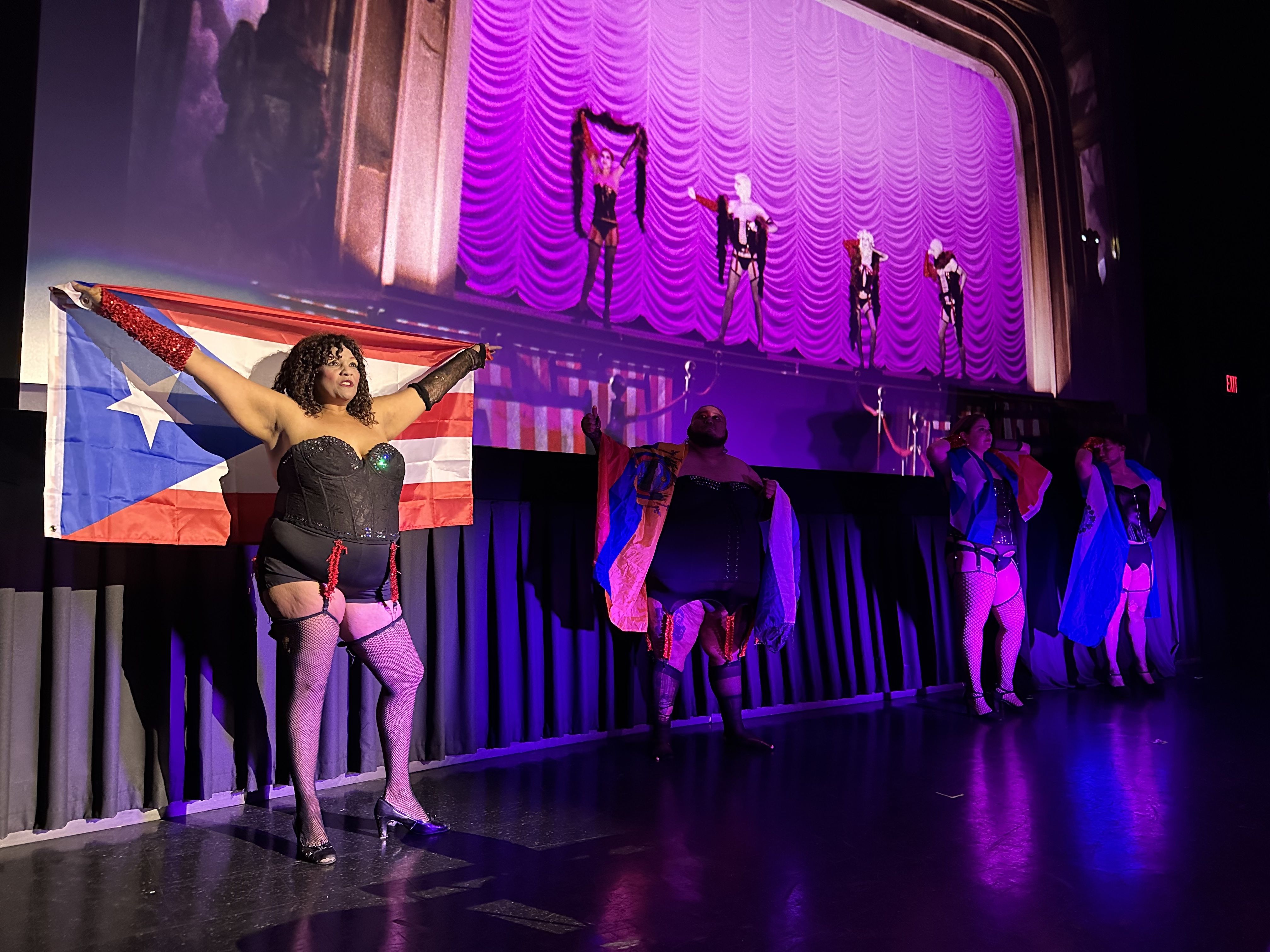 Ruthie, playing Columbia, raises a Cuban flag during an all-Latine shadowcast of Rocky Horror Picture Show in an AMC Boston Common theater.