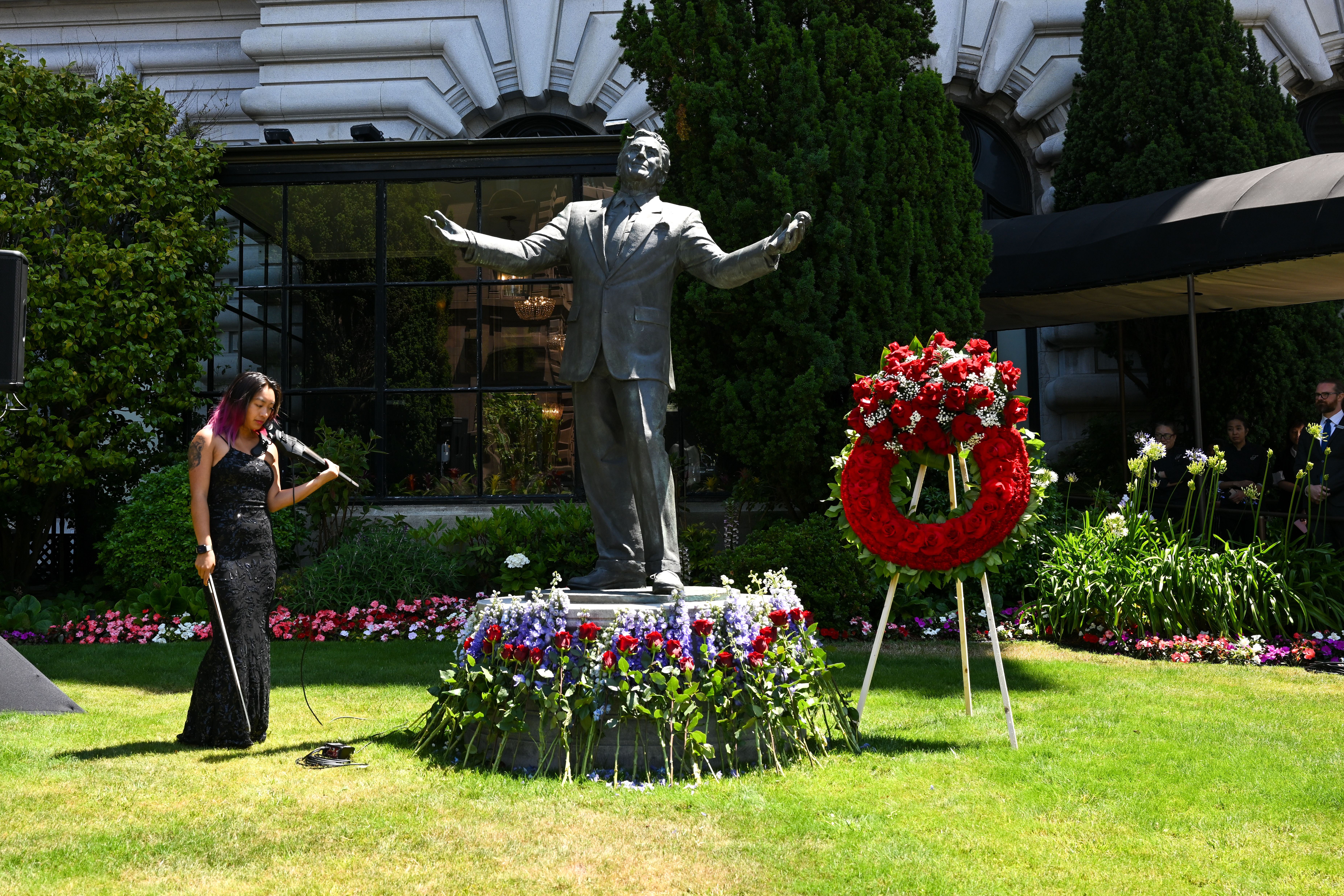 Photo of a violinist standing next to a statue of Tony Bennett on a grassy lawn