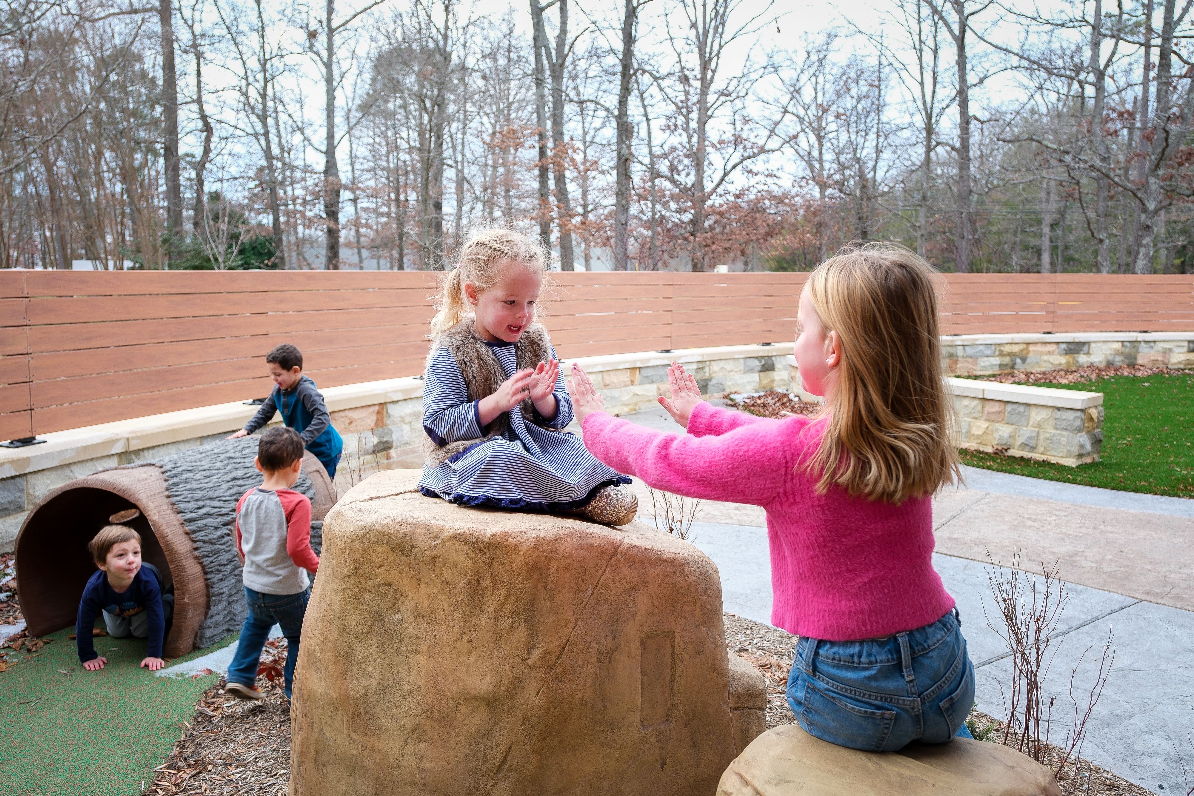 Children playing in a big library garden with climbing rocks and tunnels 