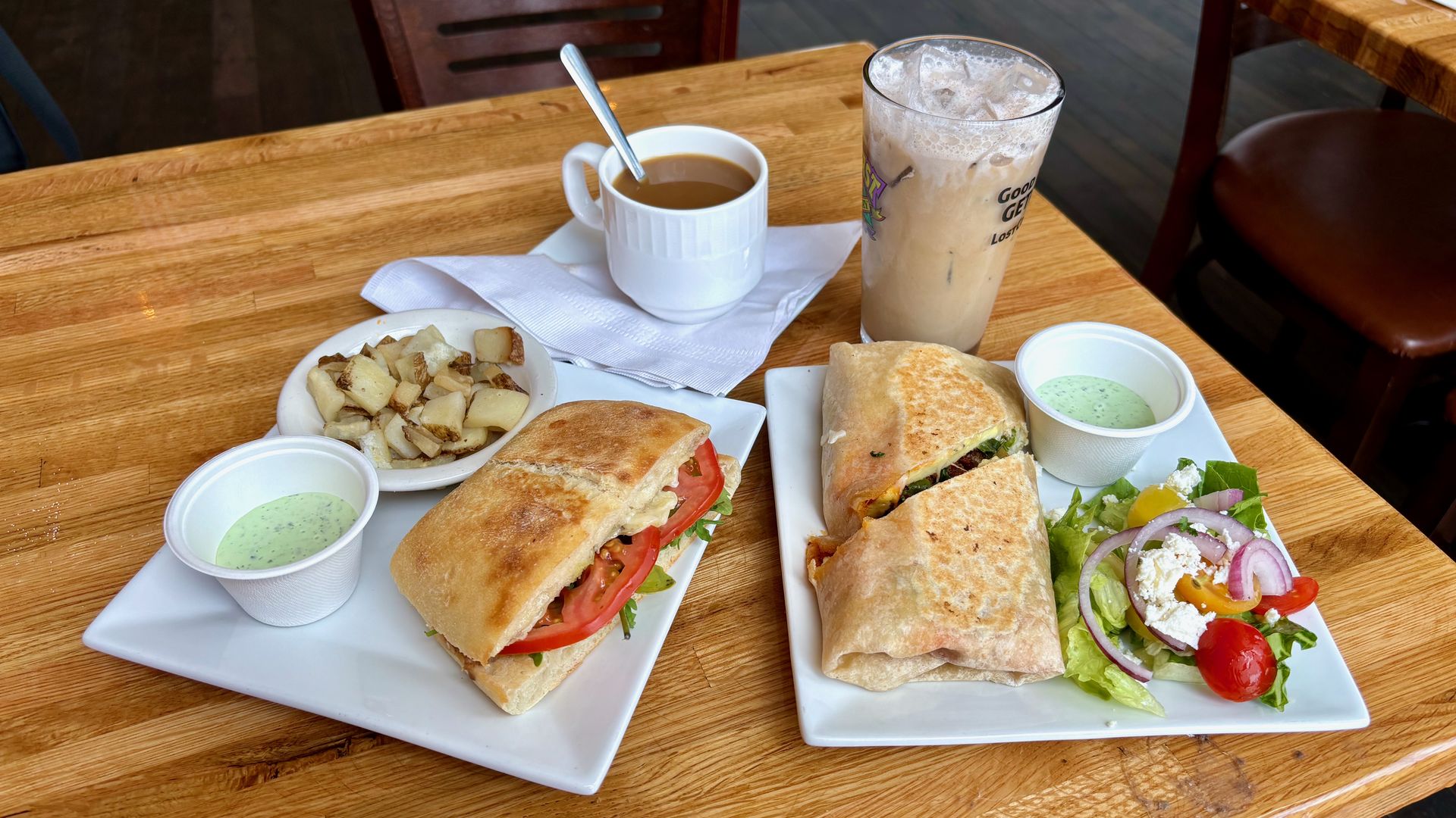 A table with two plates on it — one with a caprese sandwich and one with a breakfast burrito — and a hot and iced coffee.