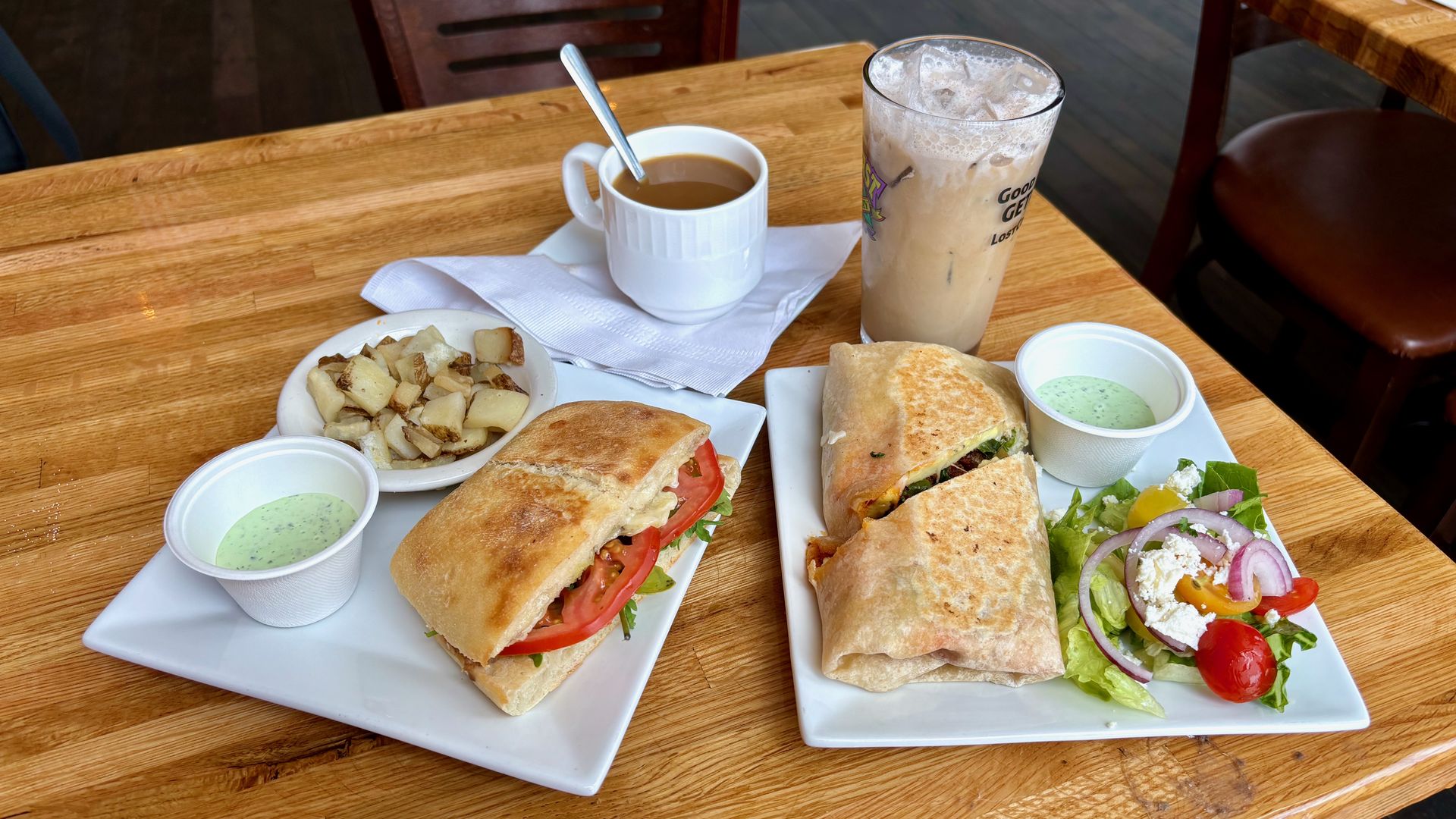 A table with two plates on it — one with a caprese sandwich and one with a breakfast burrito — and a hot and iced coffee.