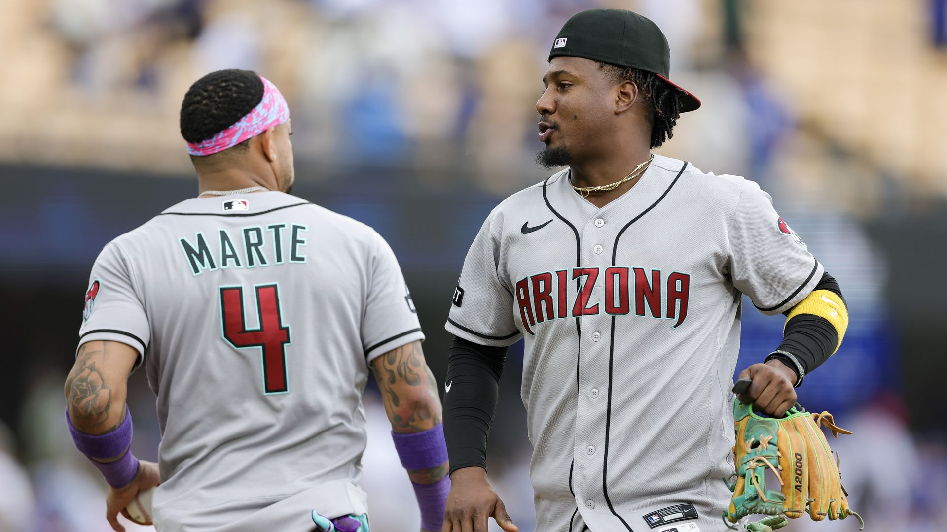 Two baseball players in off-white jerseys, one with "ARIZONA" in red letters on the front and the other with "MARTE" and the number4 on the back, slap hands and waist level on a baseball field.