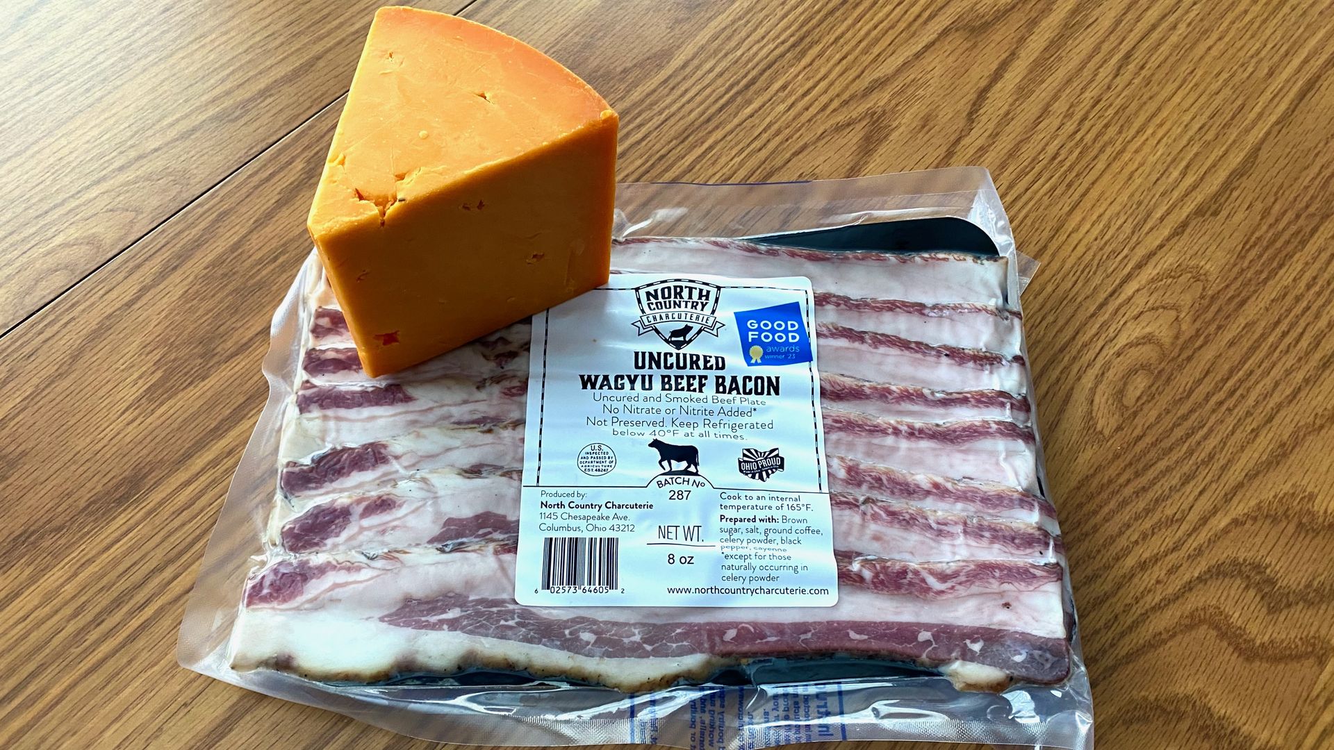 A block of cheddar cheese on top of a sealed pack of bacon