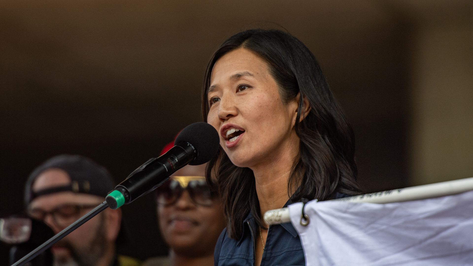 Boston Mayor Michelle Wu, wearing a blue blouse, speaks into a black microphone.
