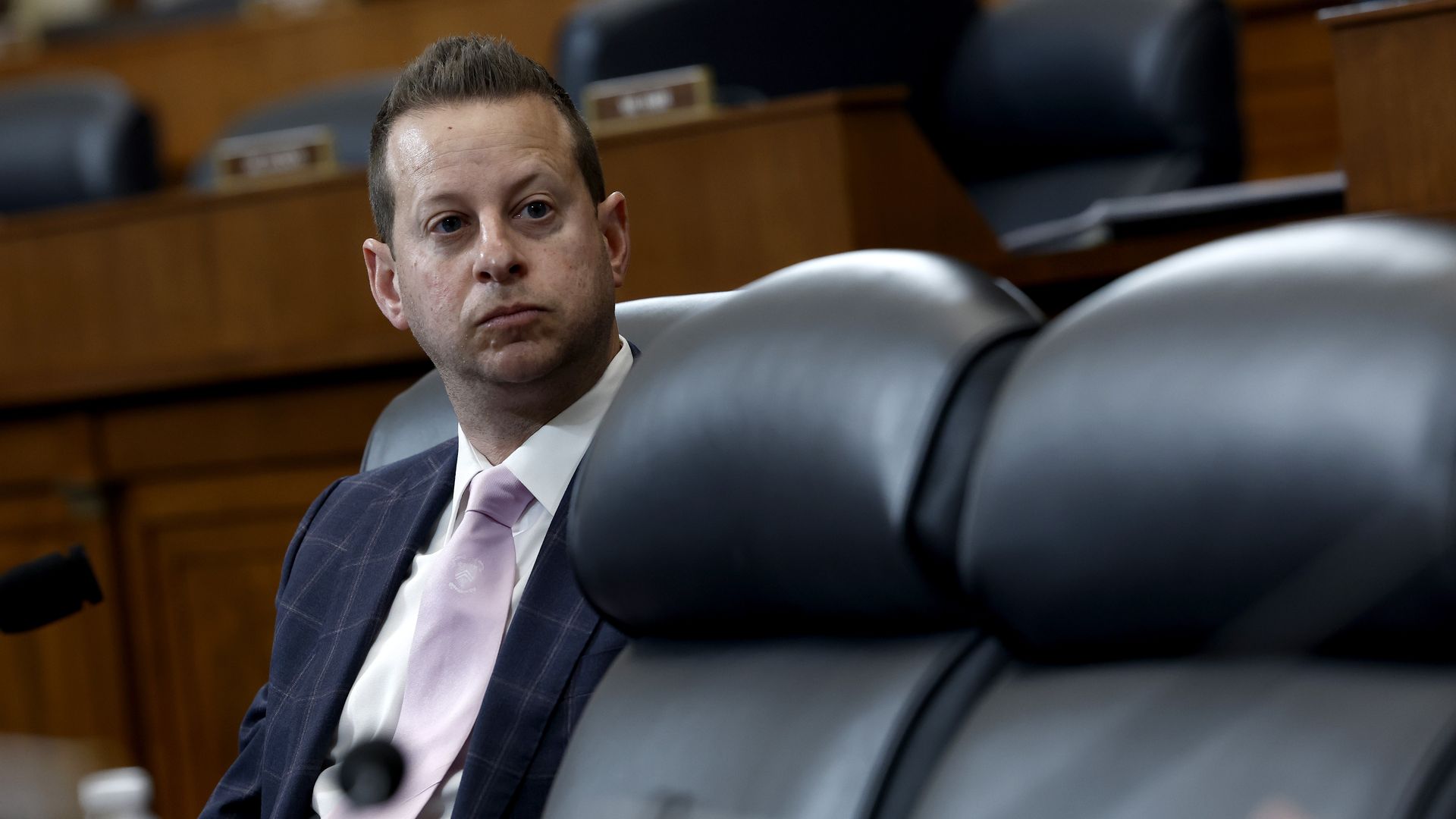 Rep. Jared Moskowitz, wearing a blue suit, white shirt and light purple tie, sitting at a committee dais.