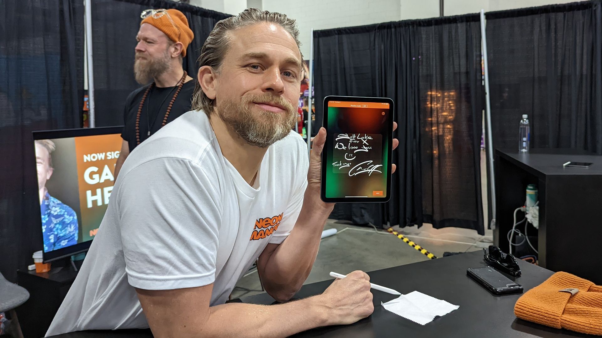 Actor Charlie Hunnam displays a digital autograph via his new company Neon Mango at FanX in Salt Lake City while his costar and cofounder Ryan Hurst walks in the background. Photo: Erin Alberty/Axios