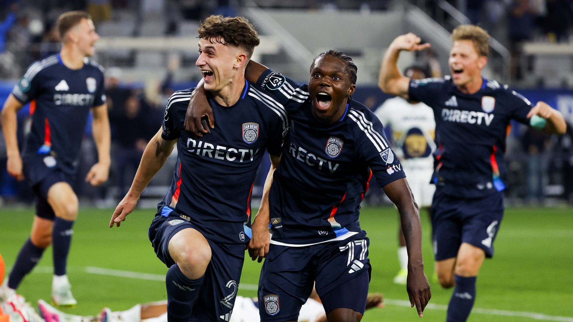 San Diego FC players hug and cheer on the field after scoring a goal at Snapdragon Stadium.
