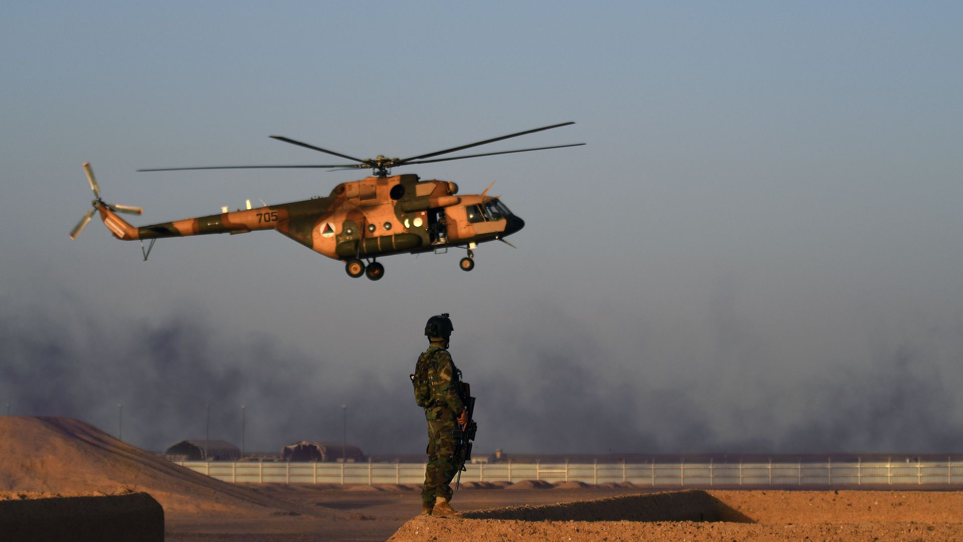 An Afghan Commando stands guard while a helicopter flies past next to Kabul's airport