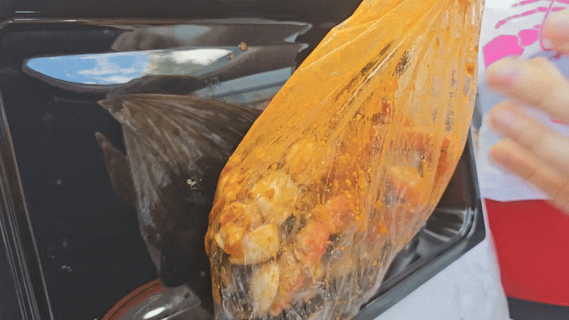 A gif of seafood being dumped into a tray, including clams, crab legs, mussels and corn.