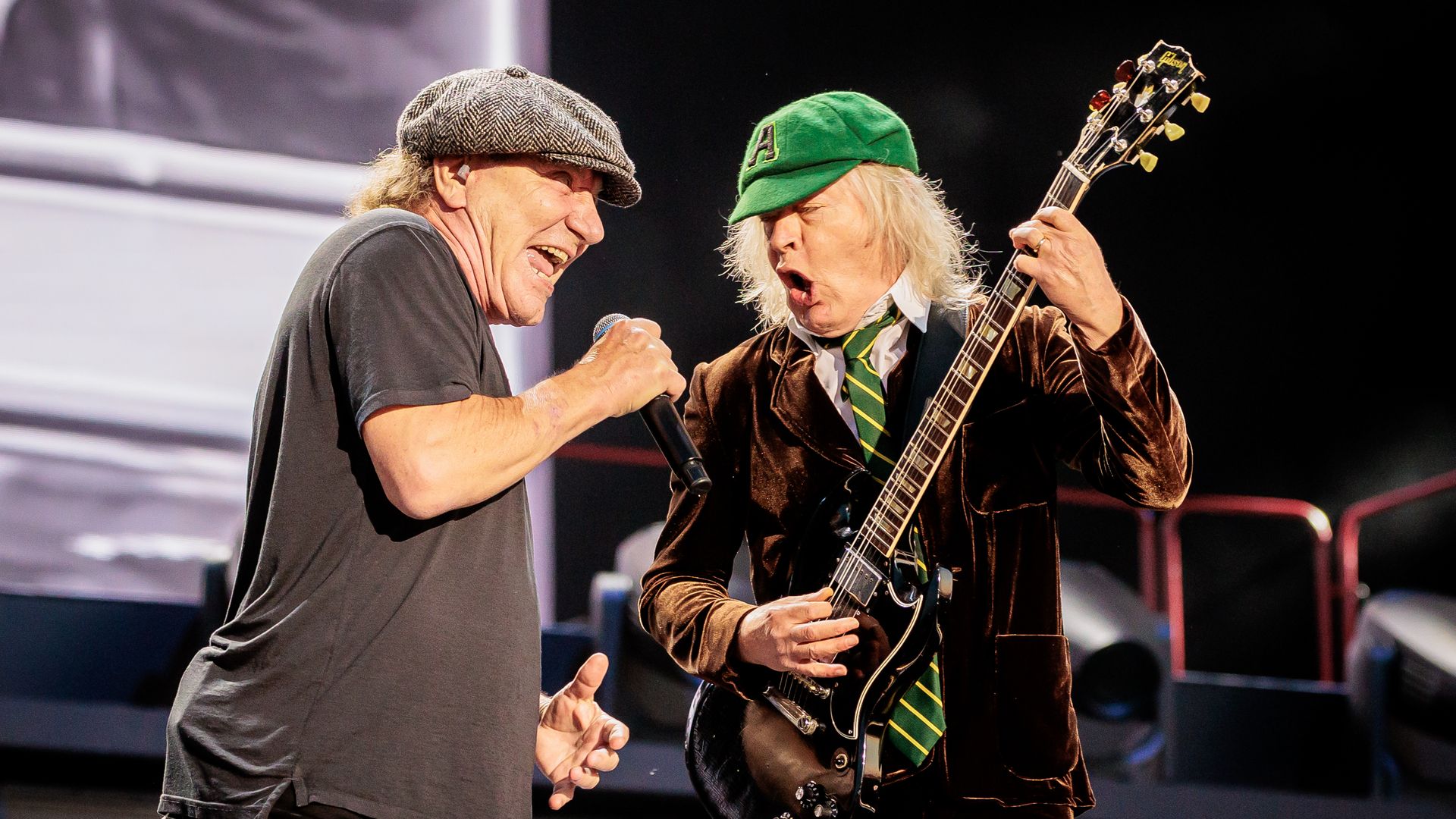 A photo of Brian Johnson and Angus Young singing and playing the guitar, respectively. 