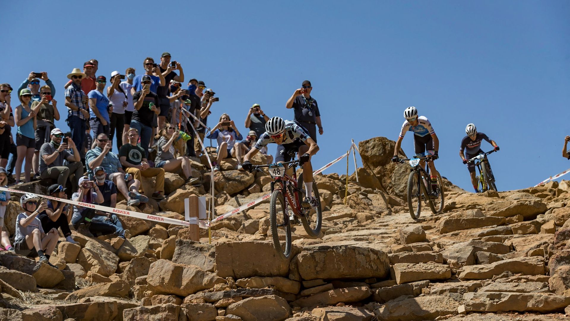 A cyclist racing competitors jumps off a rock wall on his bike. 