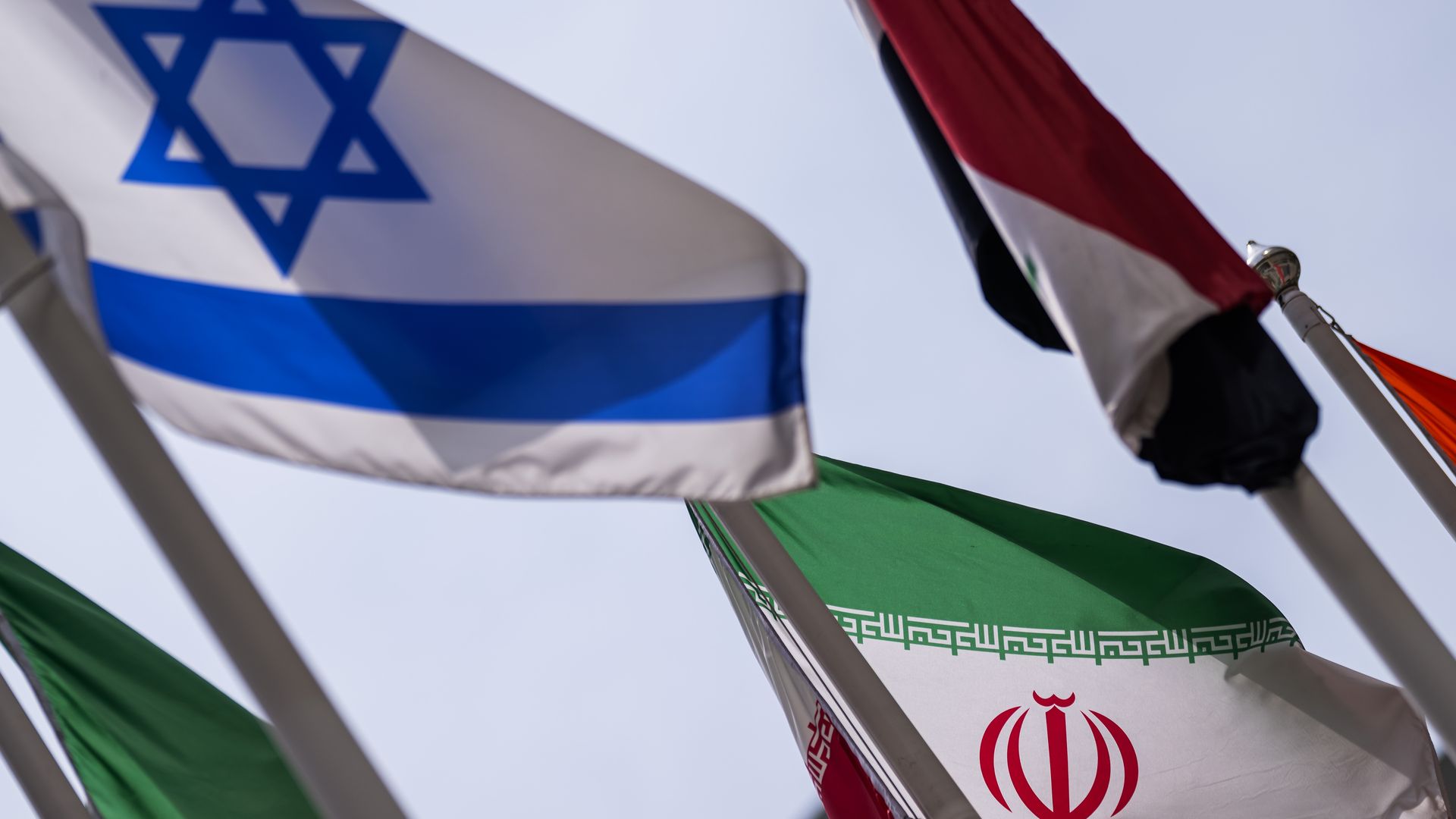 The Israeli and Iranian flags sitting under an overcast sky.