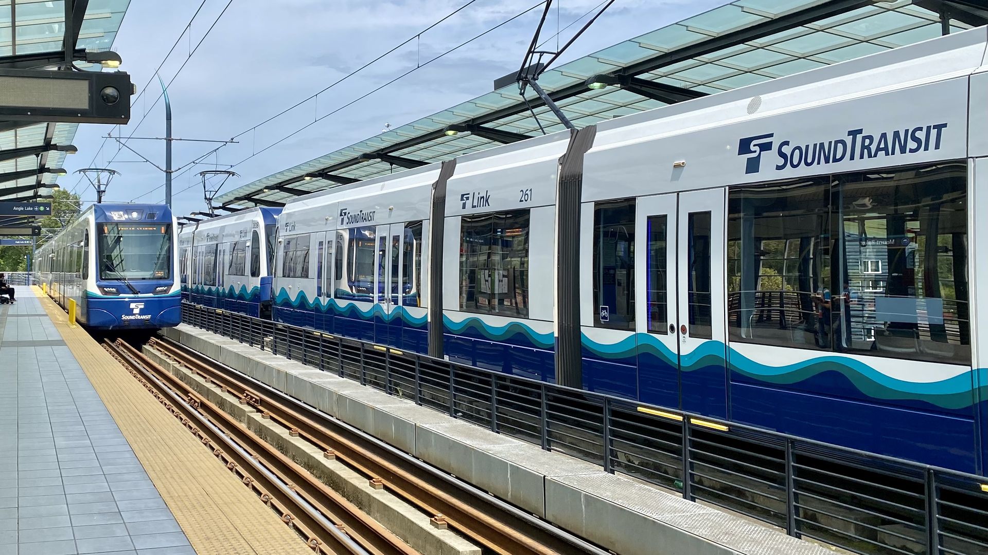 One Sound Transit light rail train pulls into a station while another pulls away. 