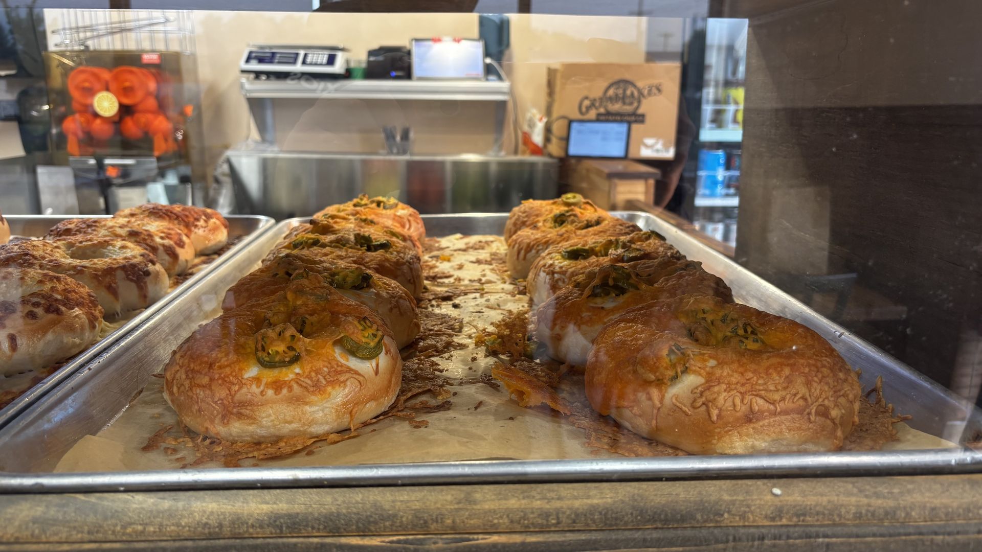 Tray of golden, cheese-topped jalapeño bagels in a bakery display case.