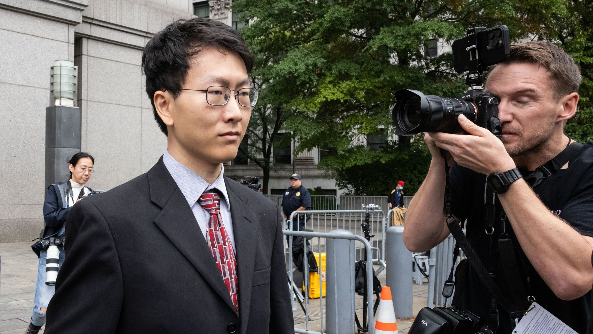 A man in a suit walks past a camera inches from his face, outside a courtroom