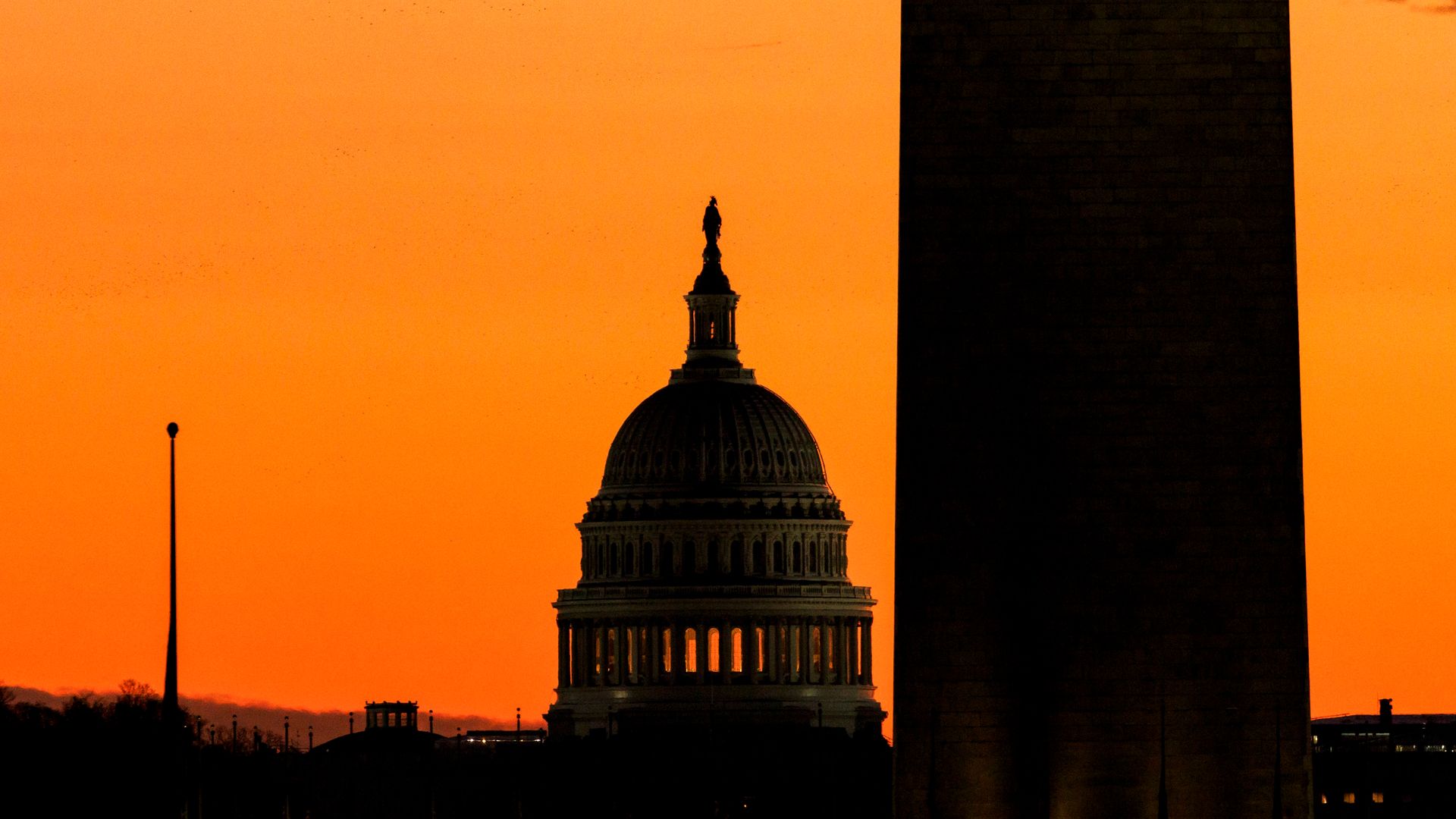 The U.S. Capitol Dome is seen in the background with the Washington Monument in the foreground beneath an orange sky.