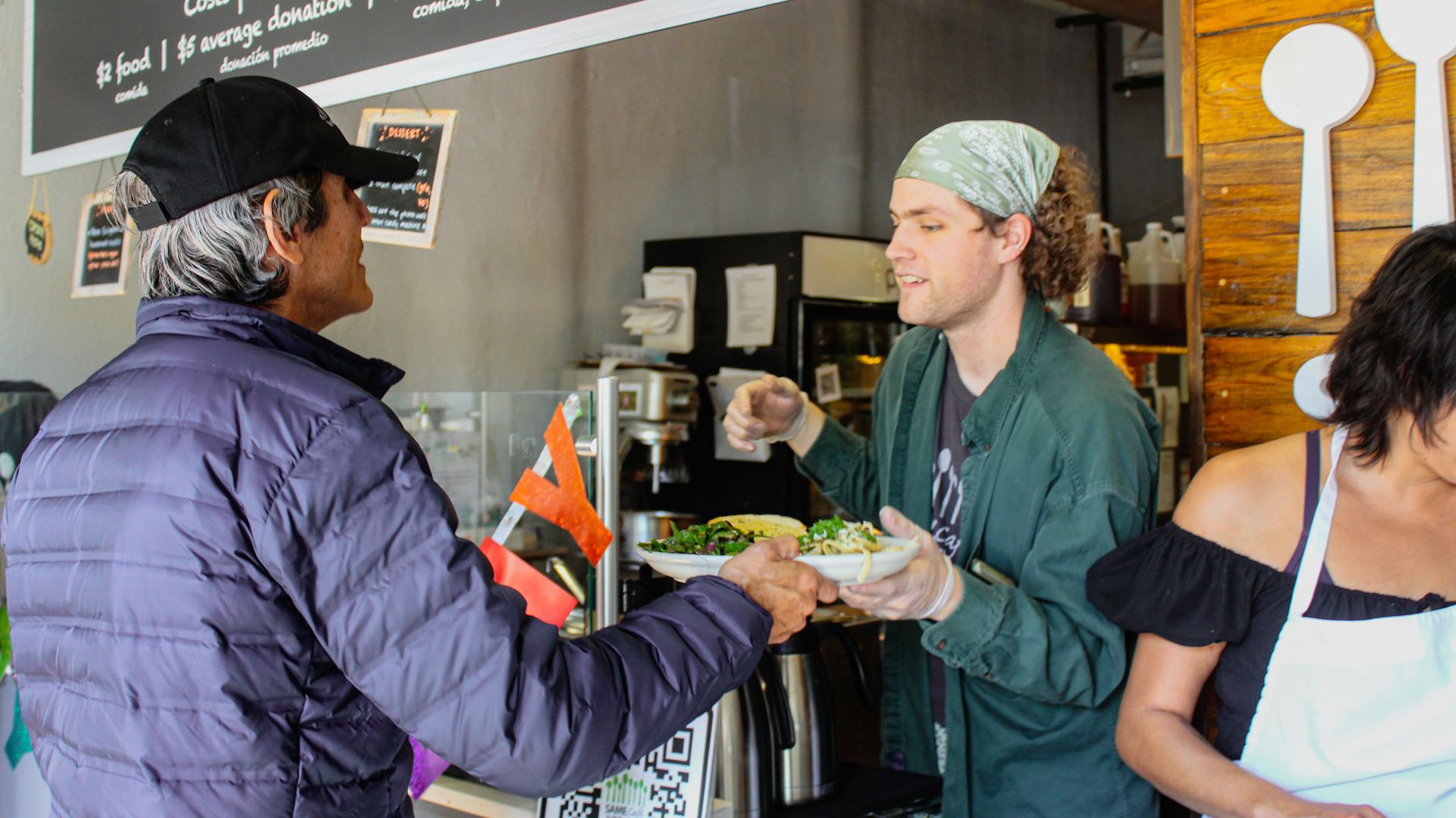 A SAME Cafe staff member hands a plate of food to a guest over the counter.