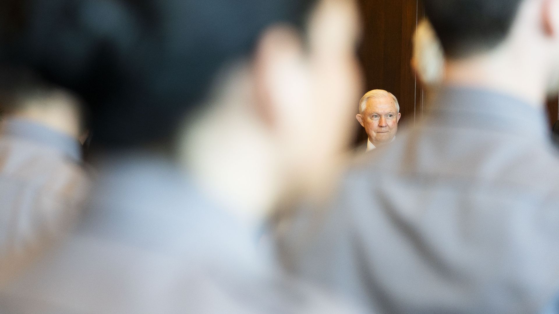 Jeff Sessions seen through a blurry foreground of men wearing grey shirts