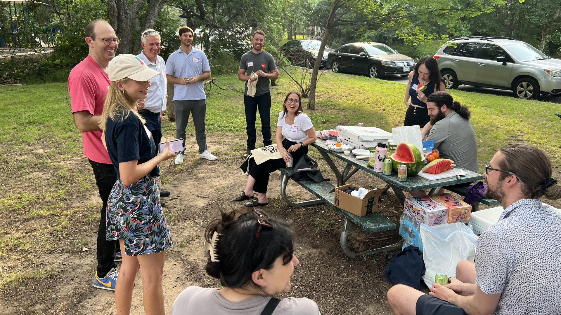 A photo of people standing around a picnic table.