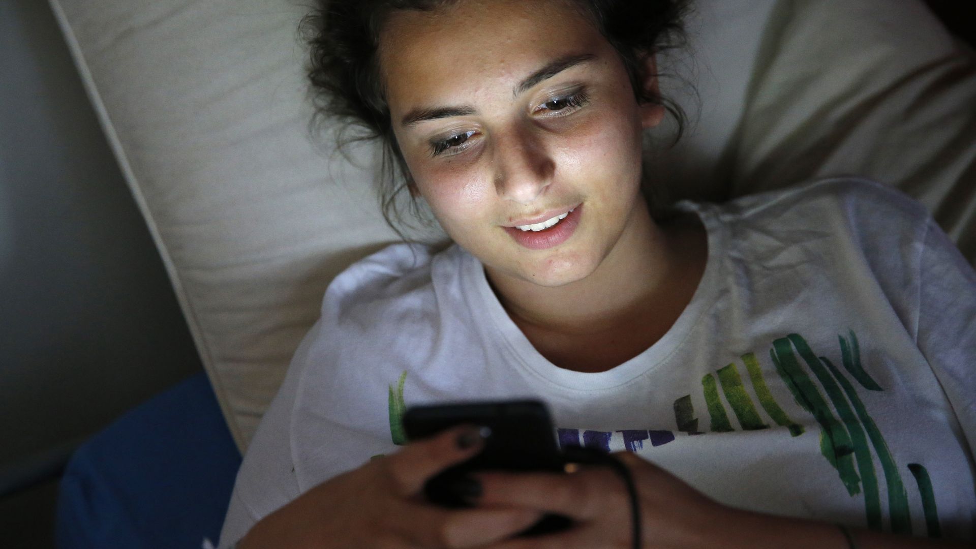 Teenager using a cell phone on her bed.