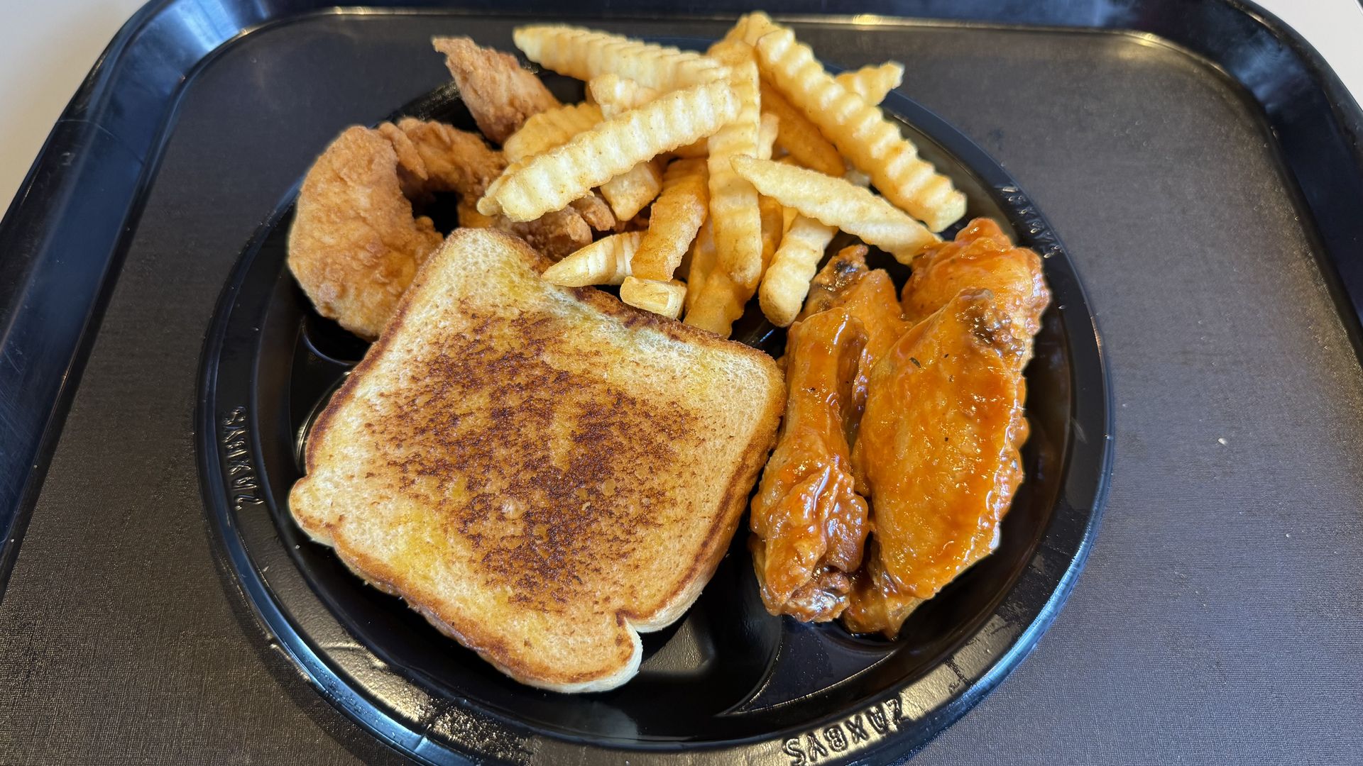 Black plate with a piece of toasted bread, crinkle-cut fries and several fried chicken fingers buffalo chicken wings on a black tray.