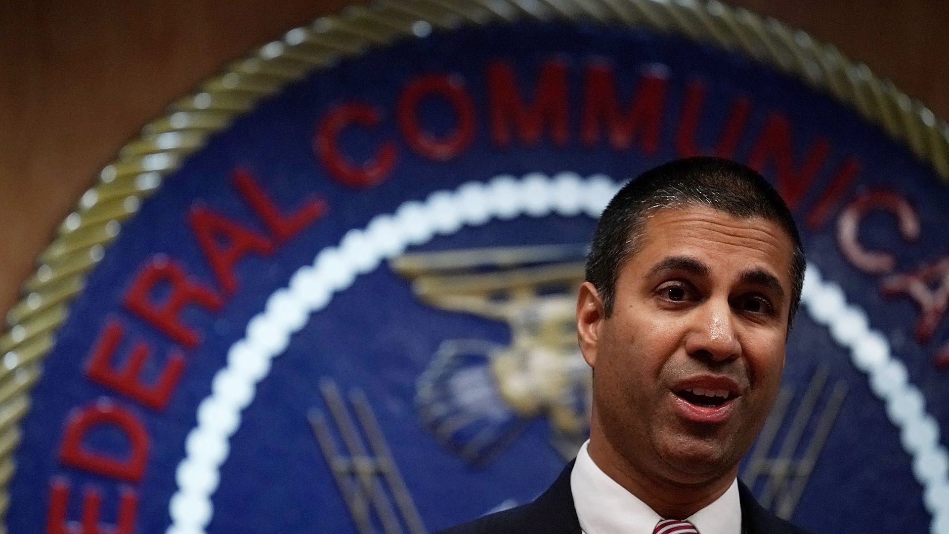 A photo of Federal Communications Commission Chairman Ajit Pai standing before the FCC's logo.