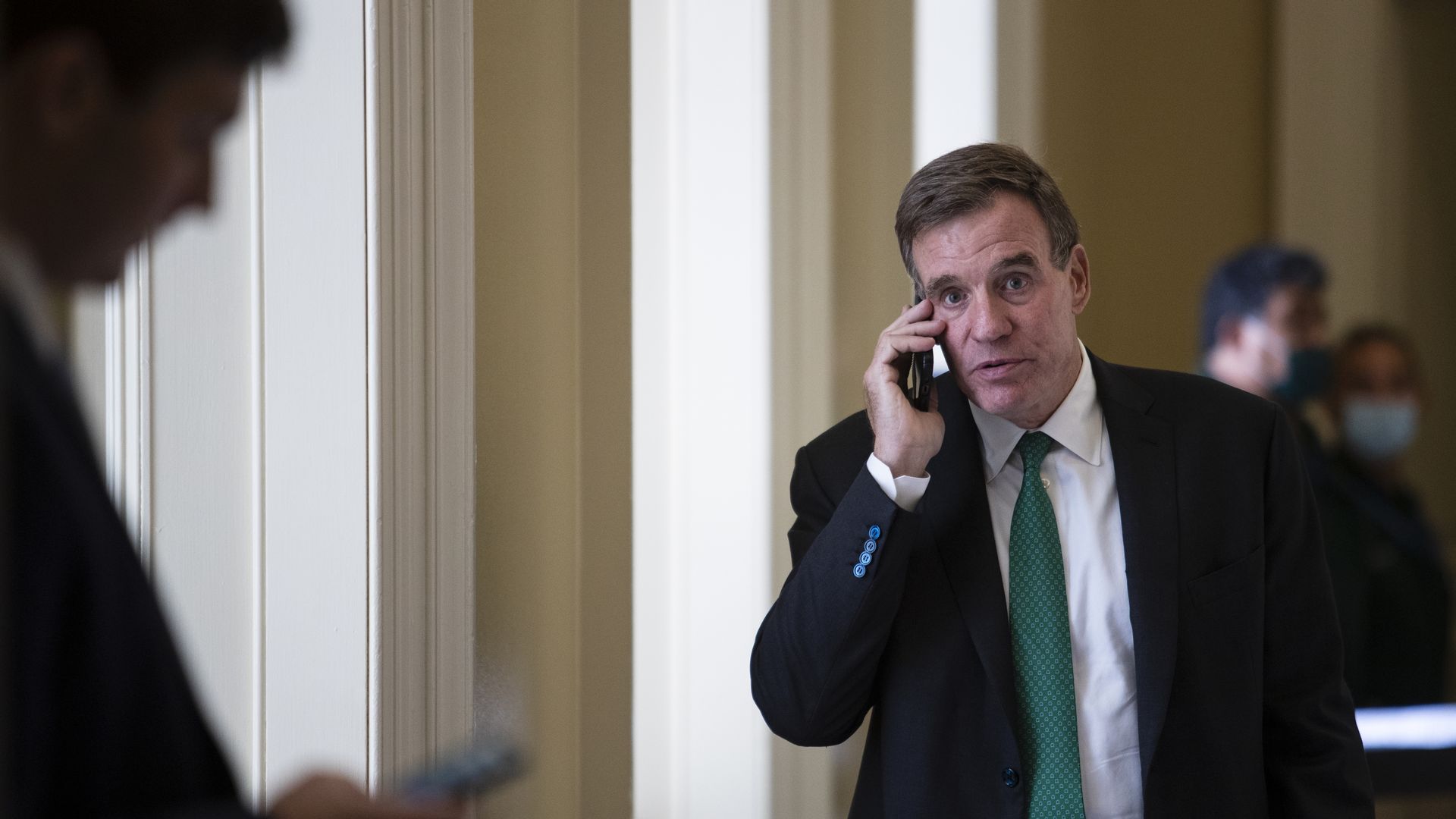 Sen. Mark Warner is seen walking through the U.S. Capitol, speaking on a cellphone.