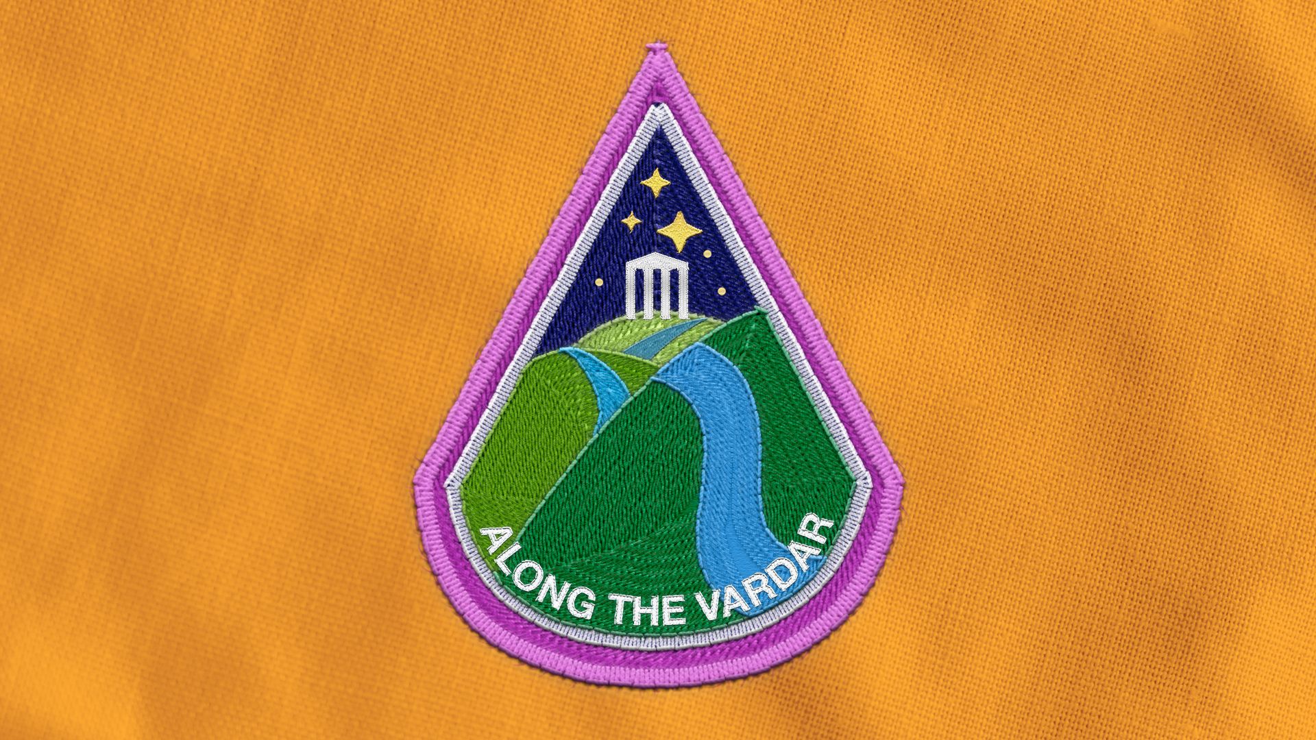 Illustration of an astronaut badge depicting a river over rolling hills with a Grecian temple in the background, the words "ALONG THE VARDAR" are on the badge.