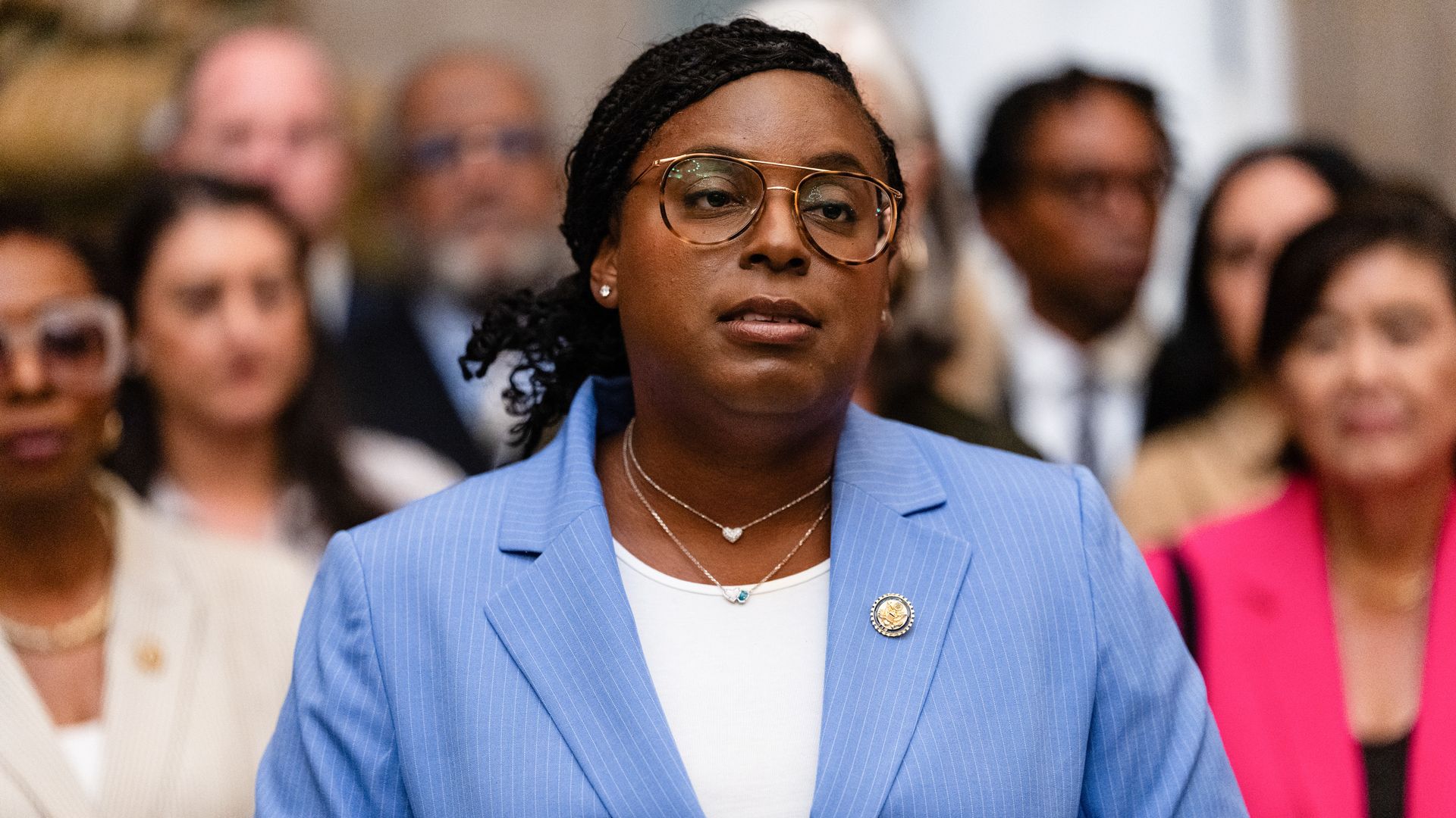 Rep. LaMonica McIver, wearing a powder blue suit and white shirt, stands in a room while flanked by Democratic colleagues.