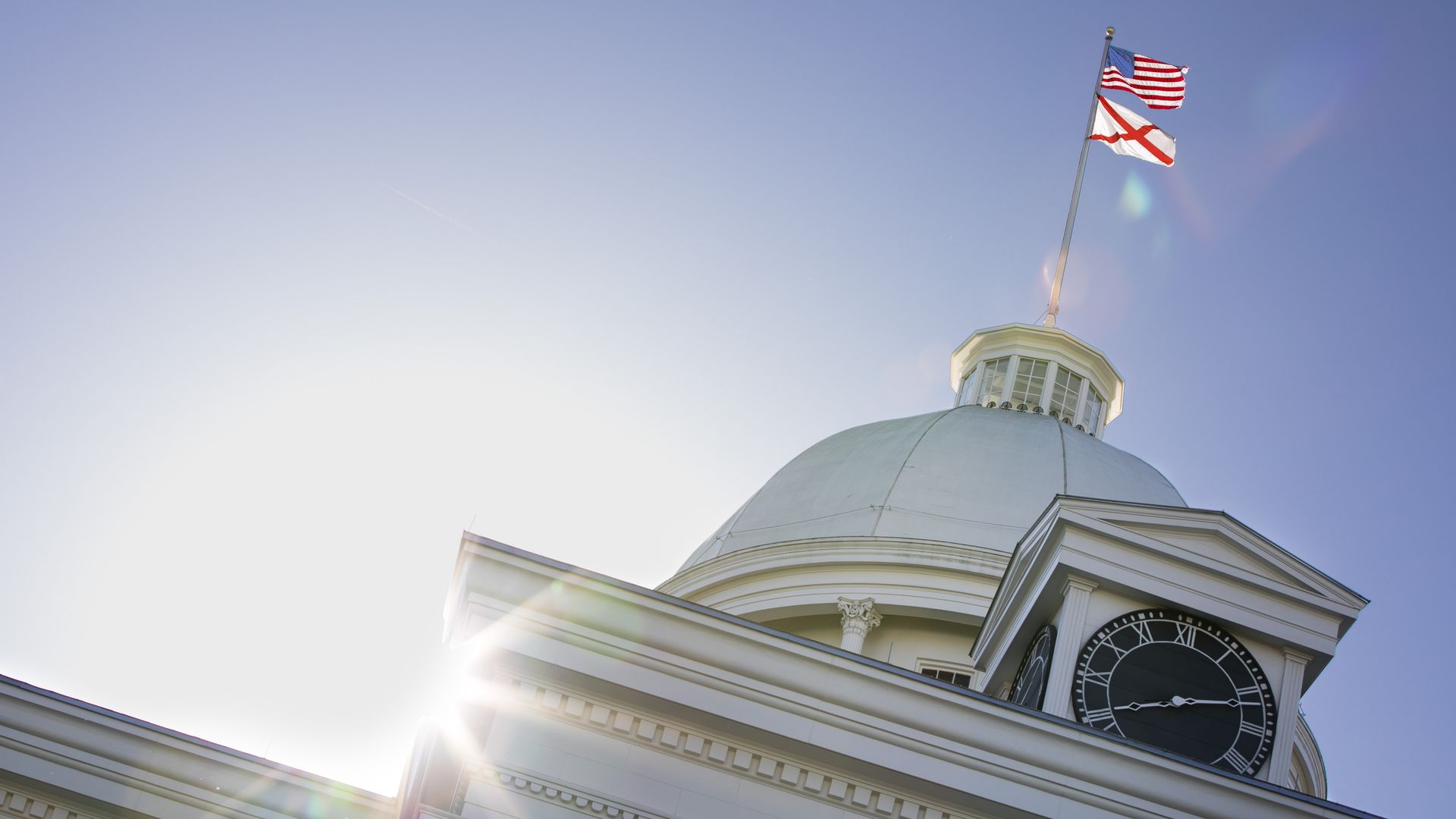 The flag of Alabama below the U.S. flag fly over a Montgomery Statehouse.