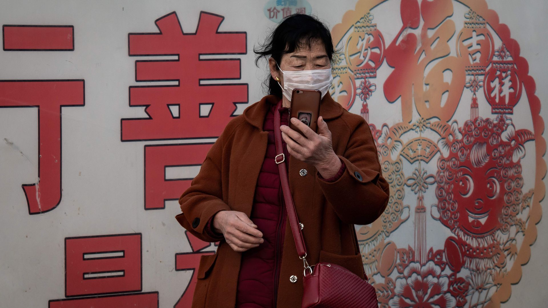 A photo of a Chinese woman wearing a face mask and looking at an iPhone