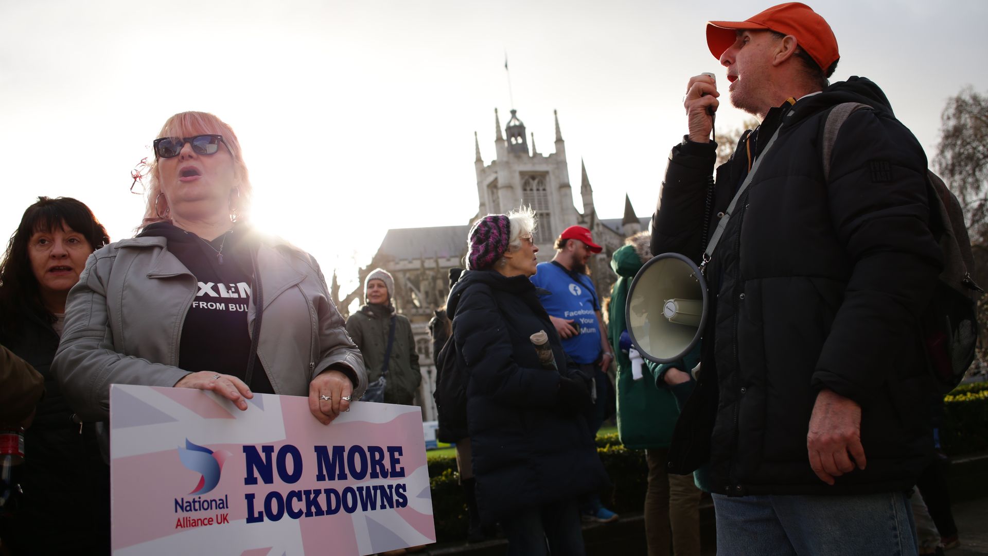 A woman holds a sign saying "no more lockdowns" next to a man in a red baseball cap 