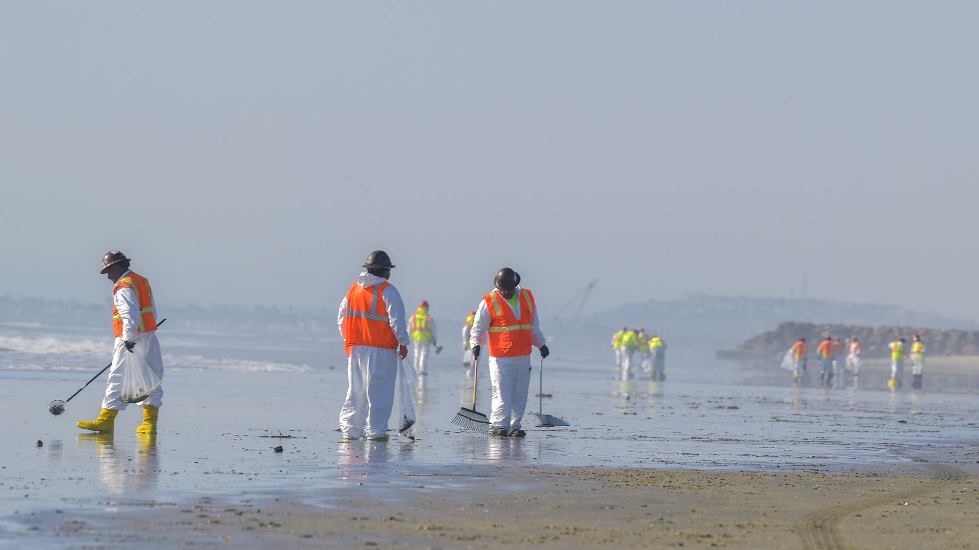 Workers search for oil in the sand at the northern end of Huntington Beach, CA, on Tuesday, October 5,