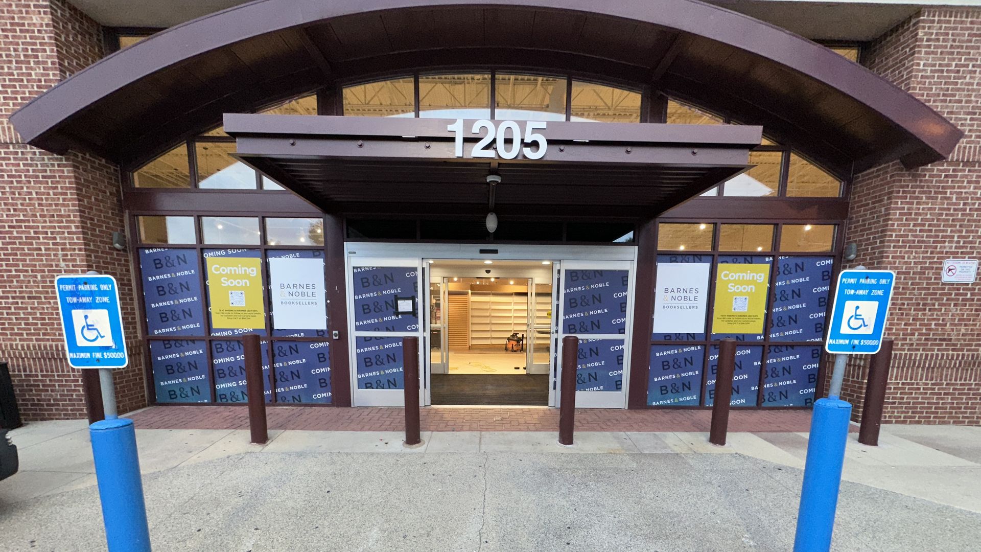 Front of Barnes & Noble at 1205: curved maroon canopy, glass doors, blue banners reading "B&N Coming Soon"; blue handicap signs in foreground.