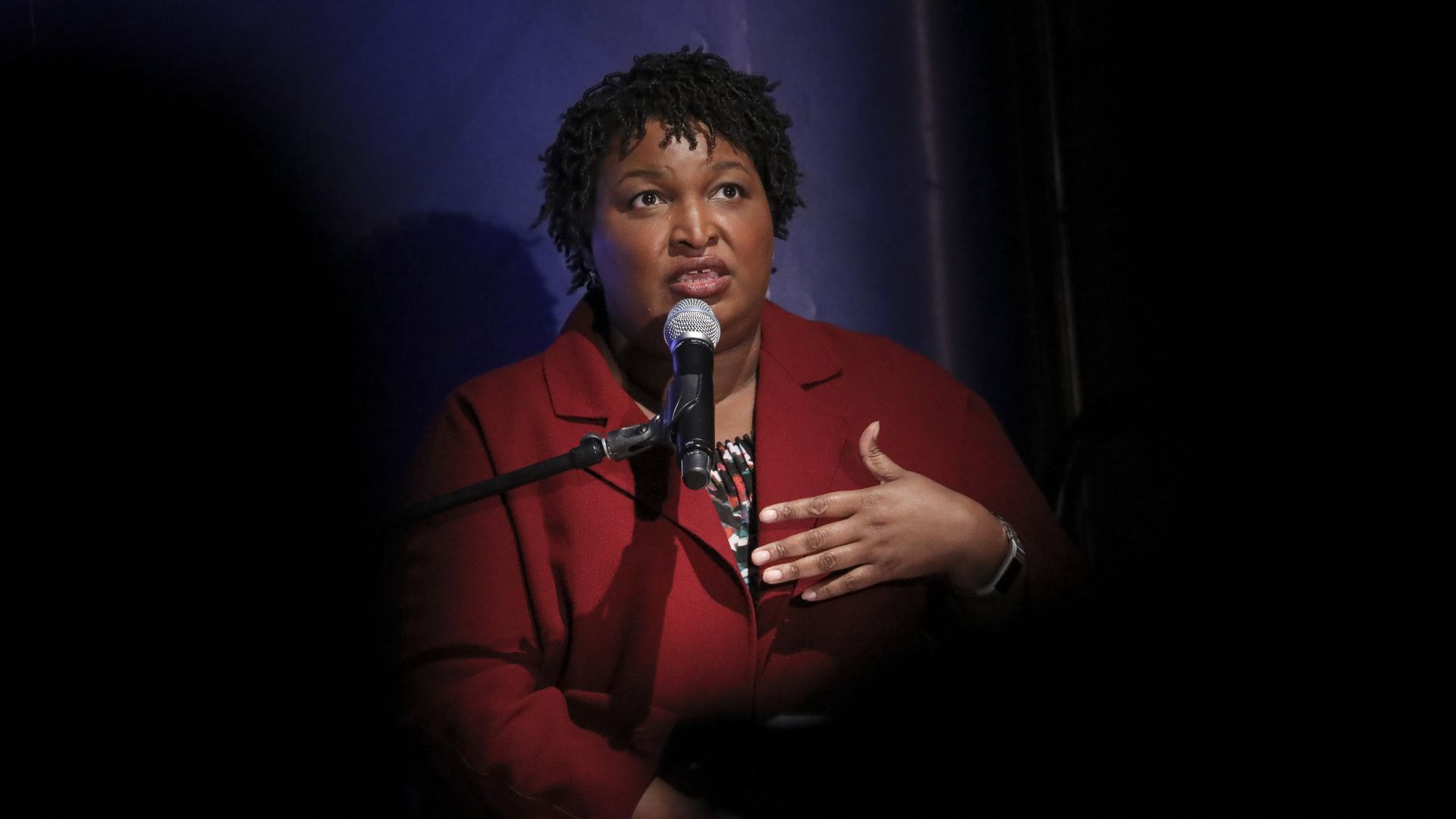 In this image, Abrams speaks into a microphone with one hand gesturing towards herself. 