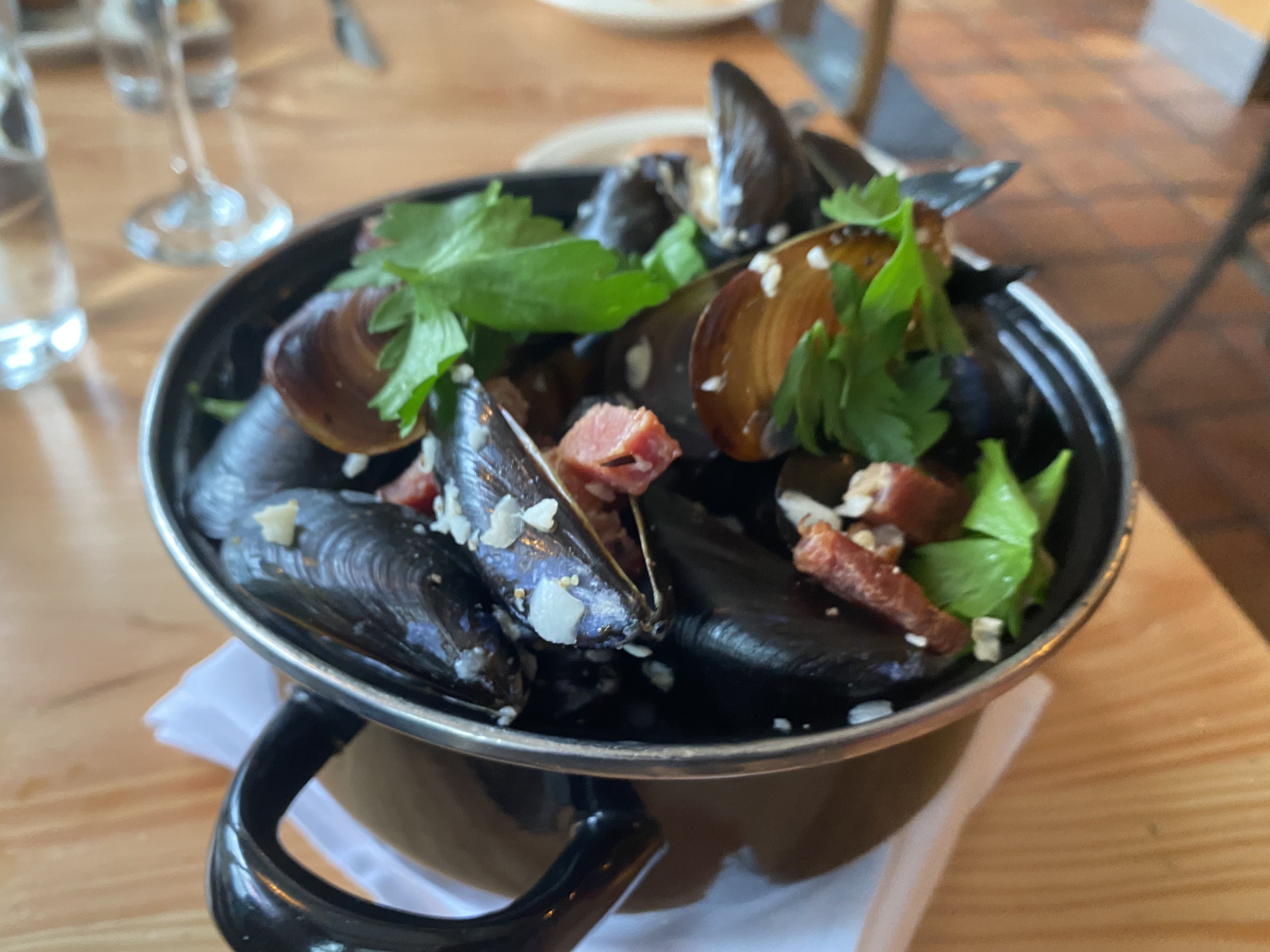 A black pot filled with mussels and studded with bits of bacon, garnished with parsley. 
