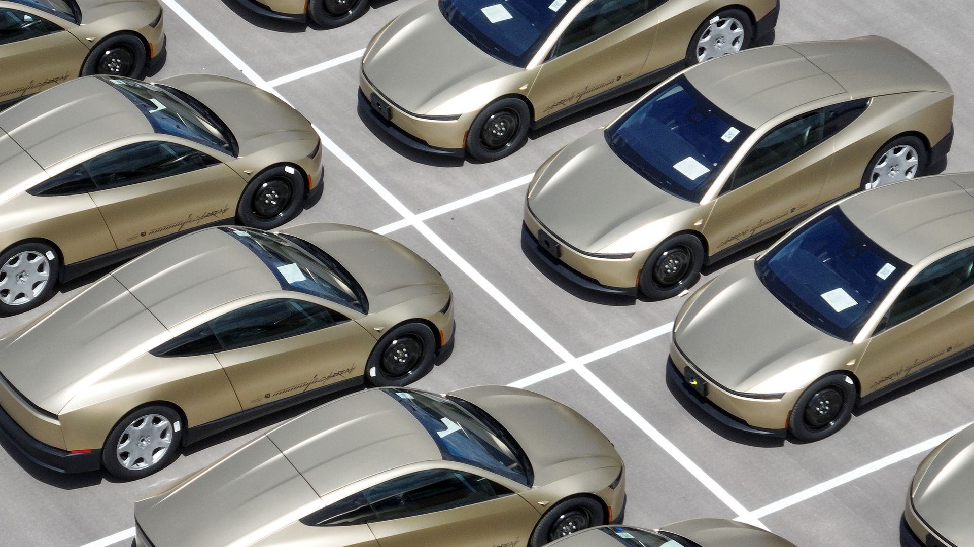 Aerial view of a parking lot filled with identical gold-colored cars arranged in diagonal rows, with white lines crisscrossing the gray pavement.
