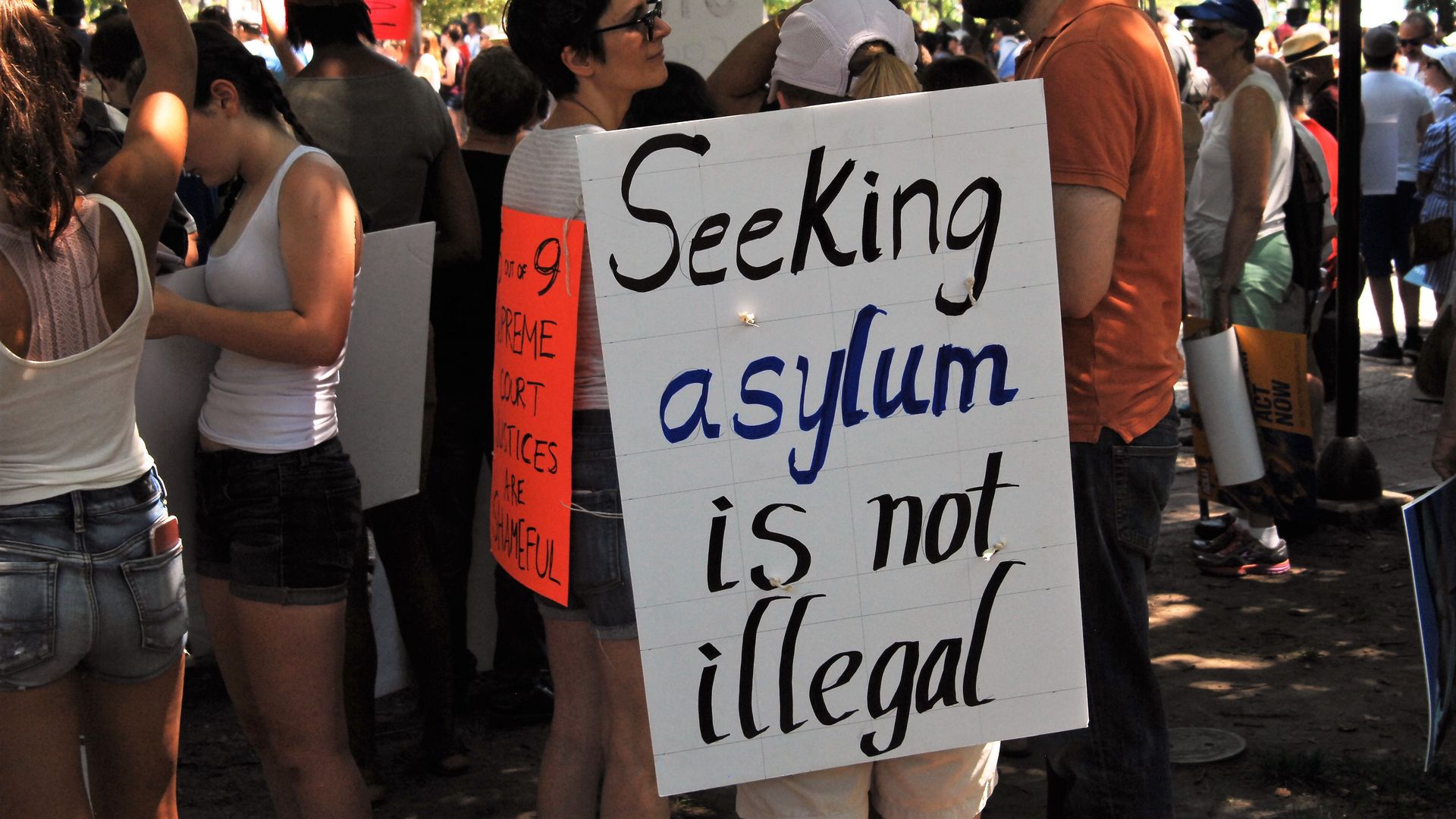 Protestors with one holding a sign that says "Seeking asylum is not illegal" 