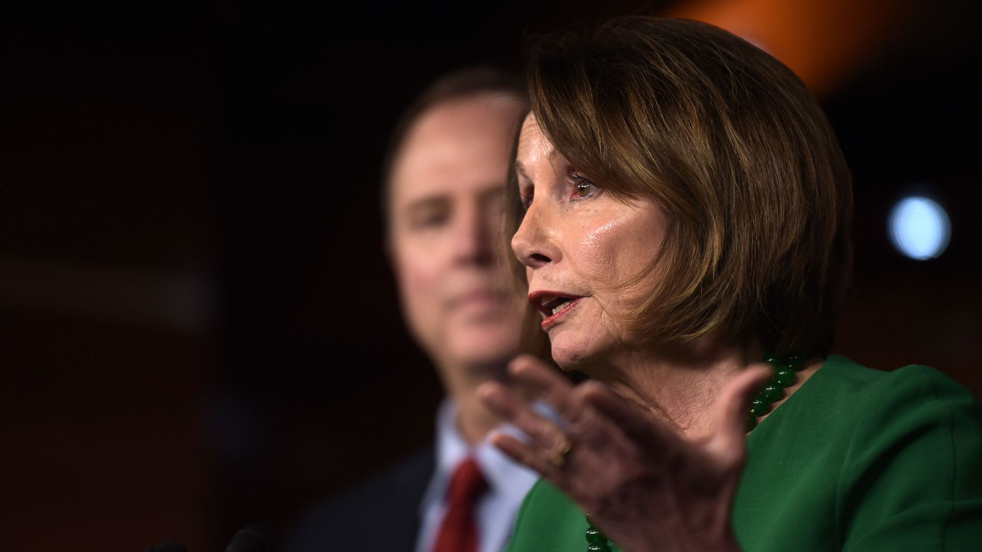 House Speaker Nancy Pelosi giving a speech on Capitol Hill wearing a green dress and holding her hand out, palm up.