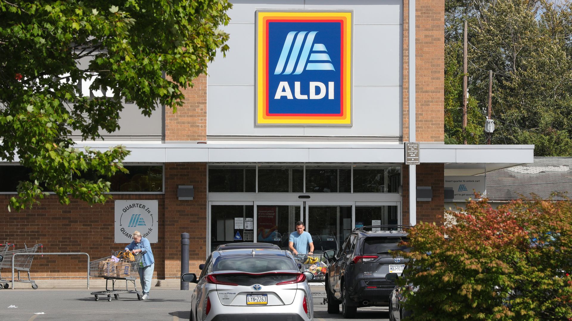 Aldi storefront with cars in parking lot and customers leaving the store.