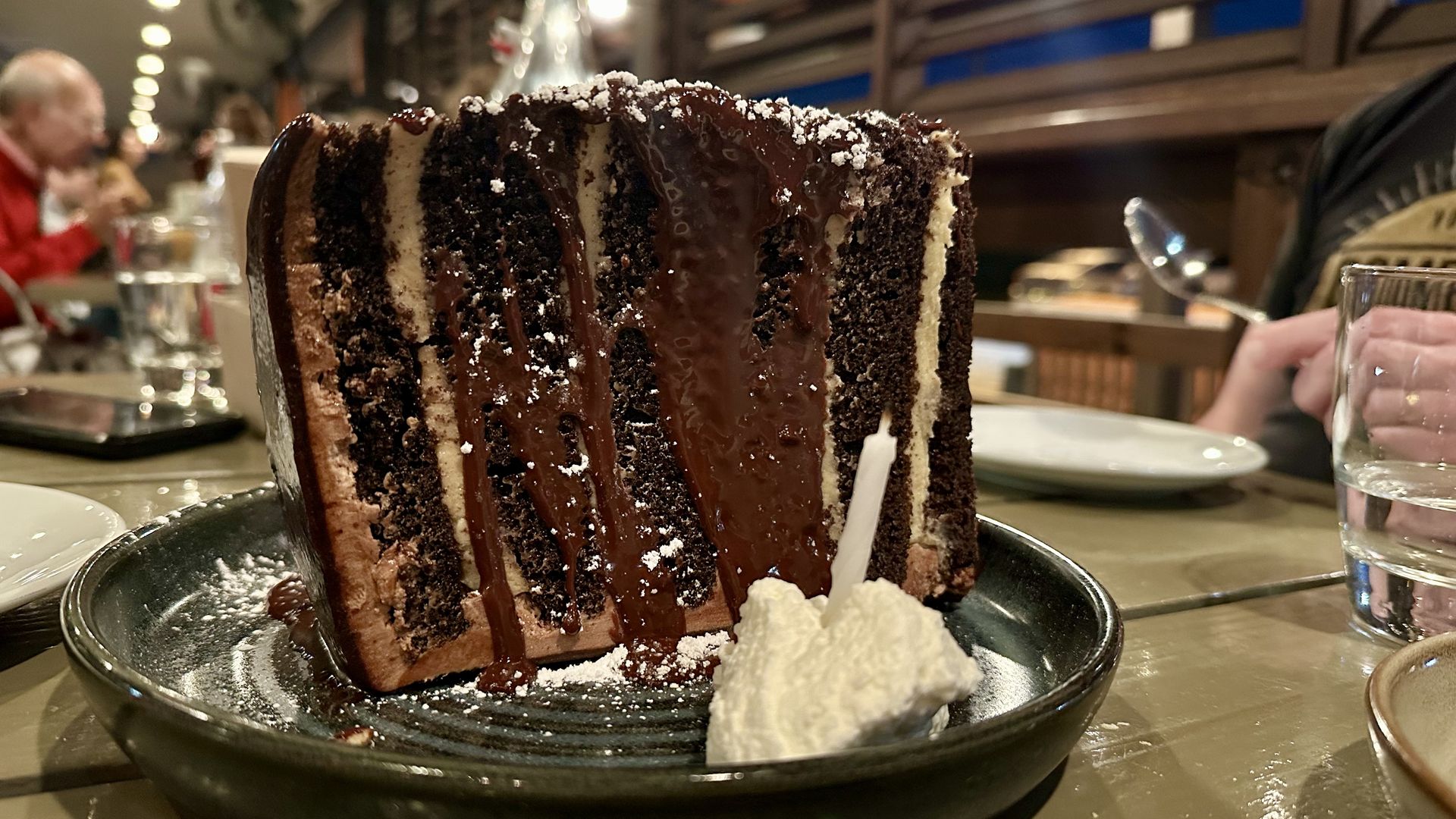 Photo shows a tall piece of chocolate peanut butter doberge cake on a plate
