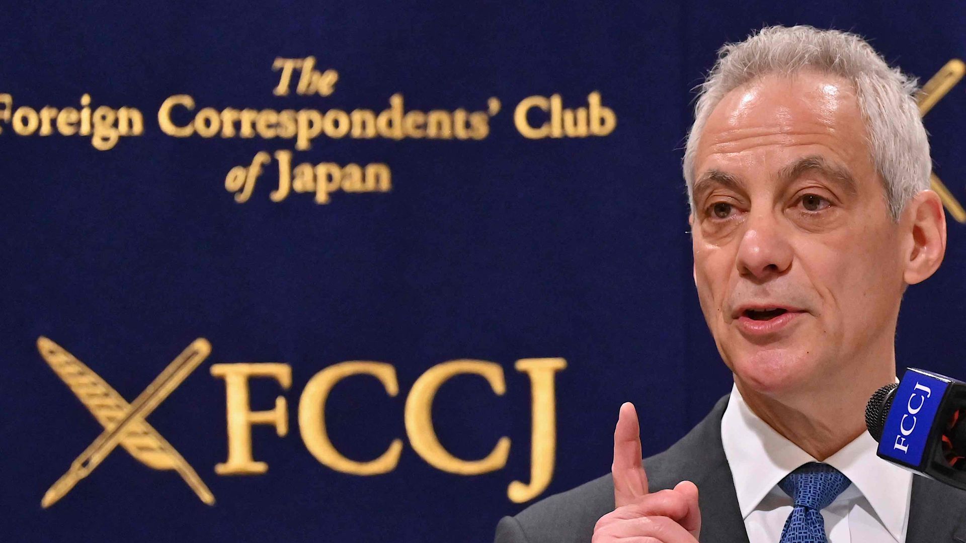 Rahm Emanuel speaks into a microphone and points a finger up