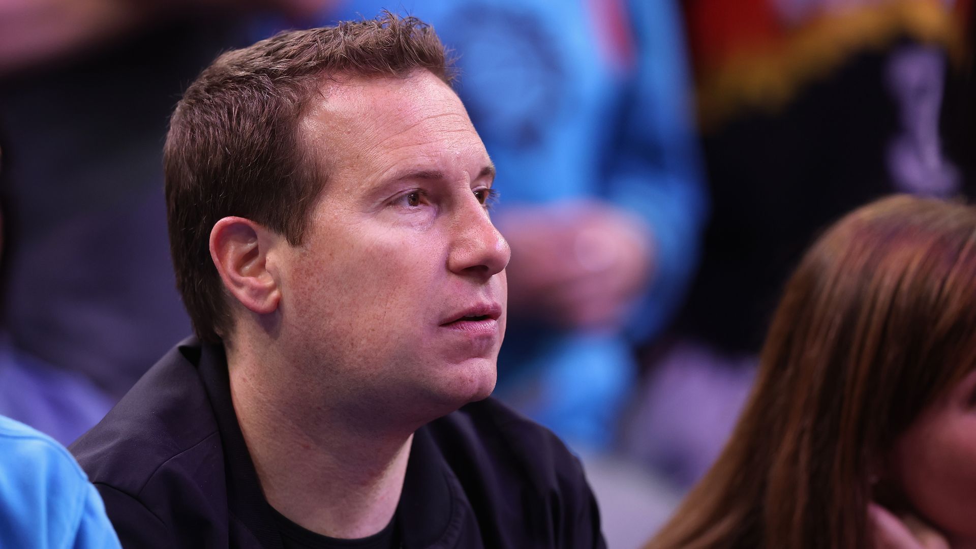 A man with short-cropped brown hair watches a basketball game
