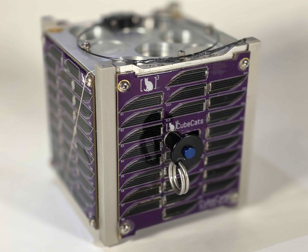 Small purple front-panel server with vented grills and a silver frame. A black lock with a blue knob and key ring hangs on the front; top shows a circular disk labeled iCubeCats.