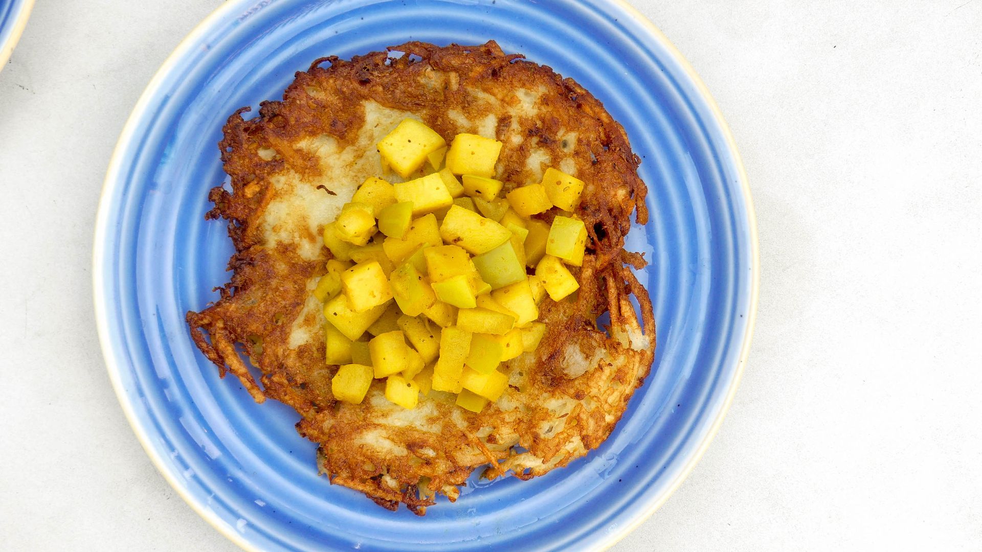 A latke on a blue plate with diced apple on top 