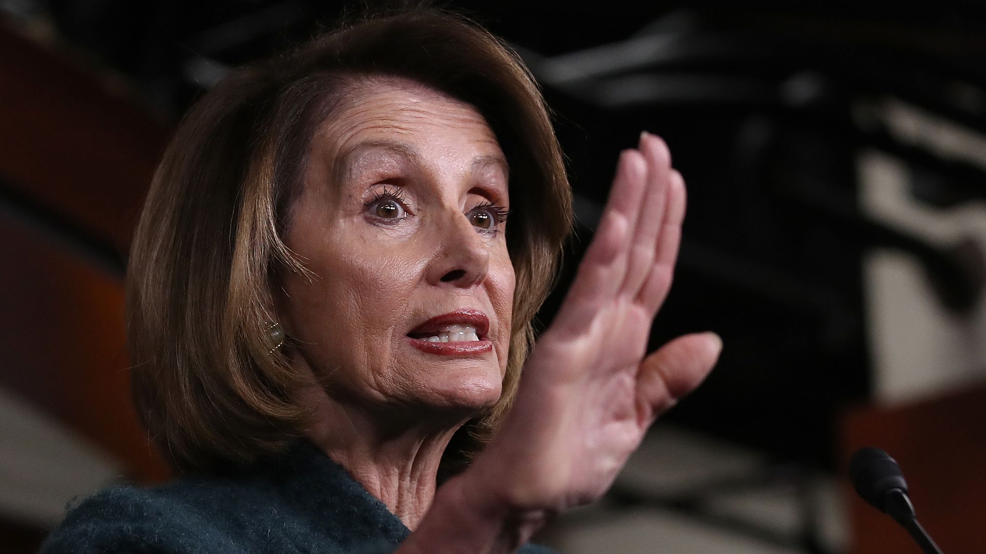 In this image, Pelosi speaks and holds up a hand.